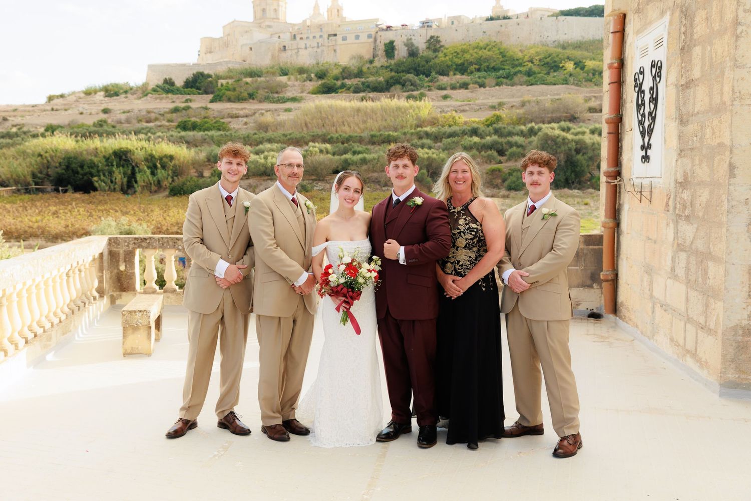 Wedding party members show off their shoes while sitting on a stone wall at an outdoor venue.