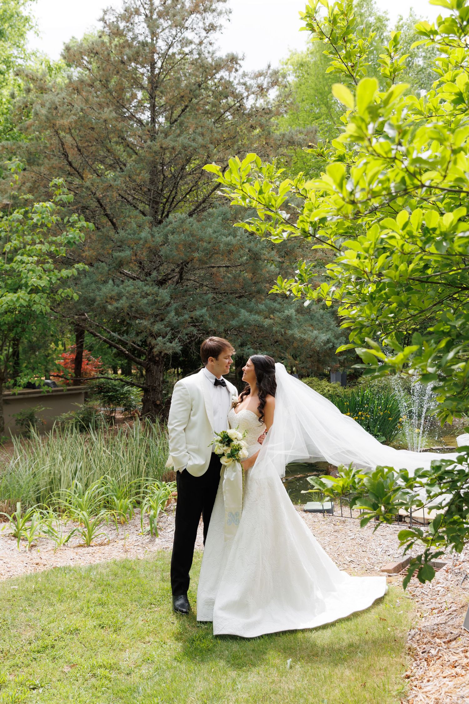 Bride and groom share a romantic moment in a lush garden, her veil flowing in the breeze.