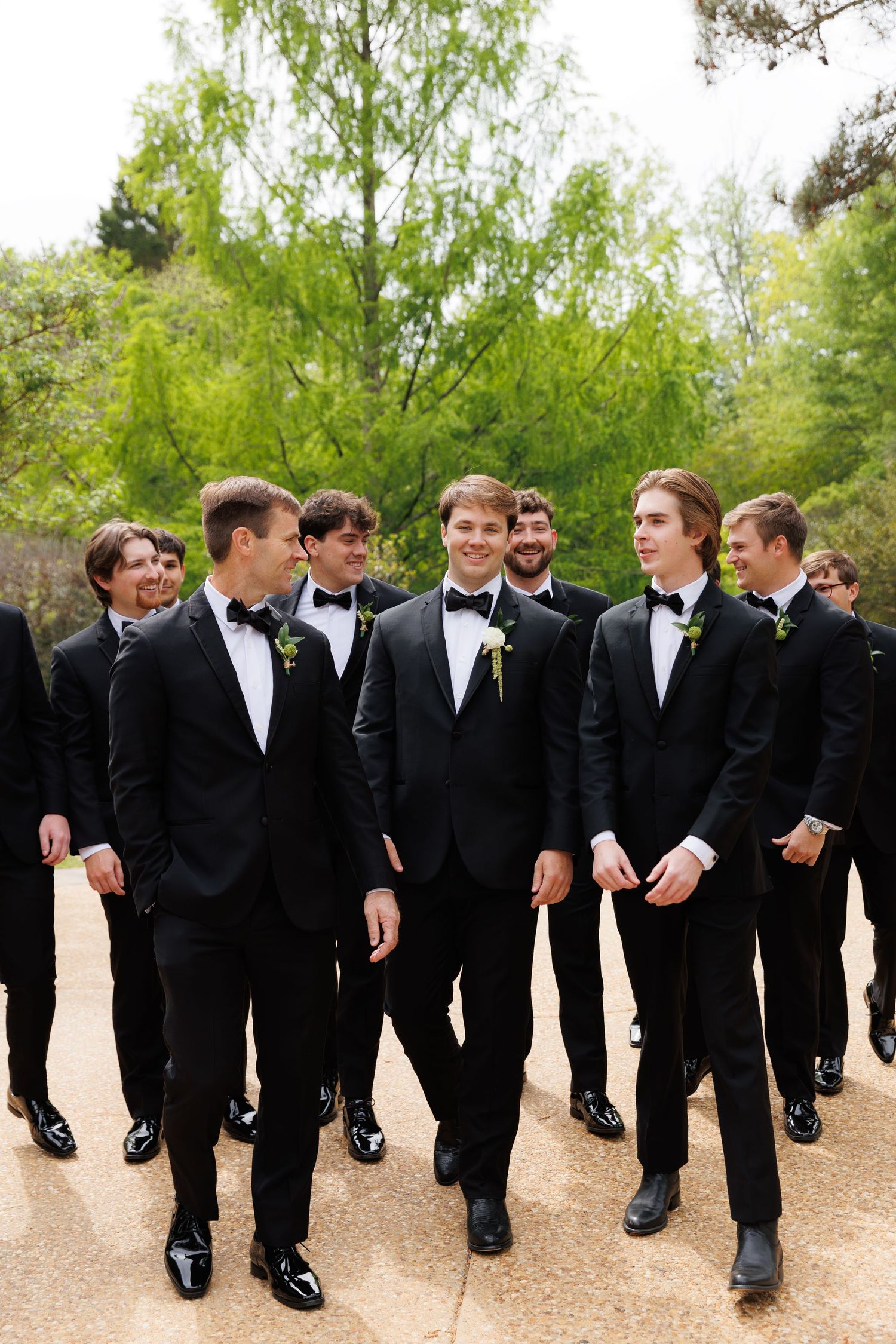 Groomsmen in black tuxedos with boutonnieres walking together outdoors at a wedding.