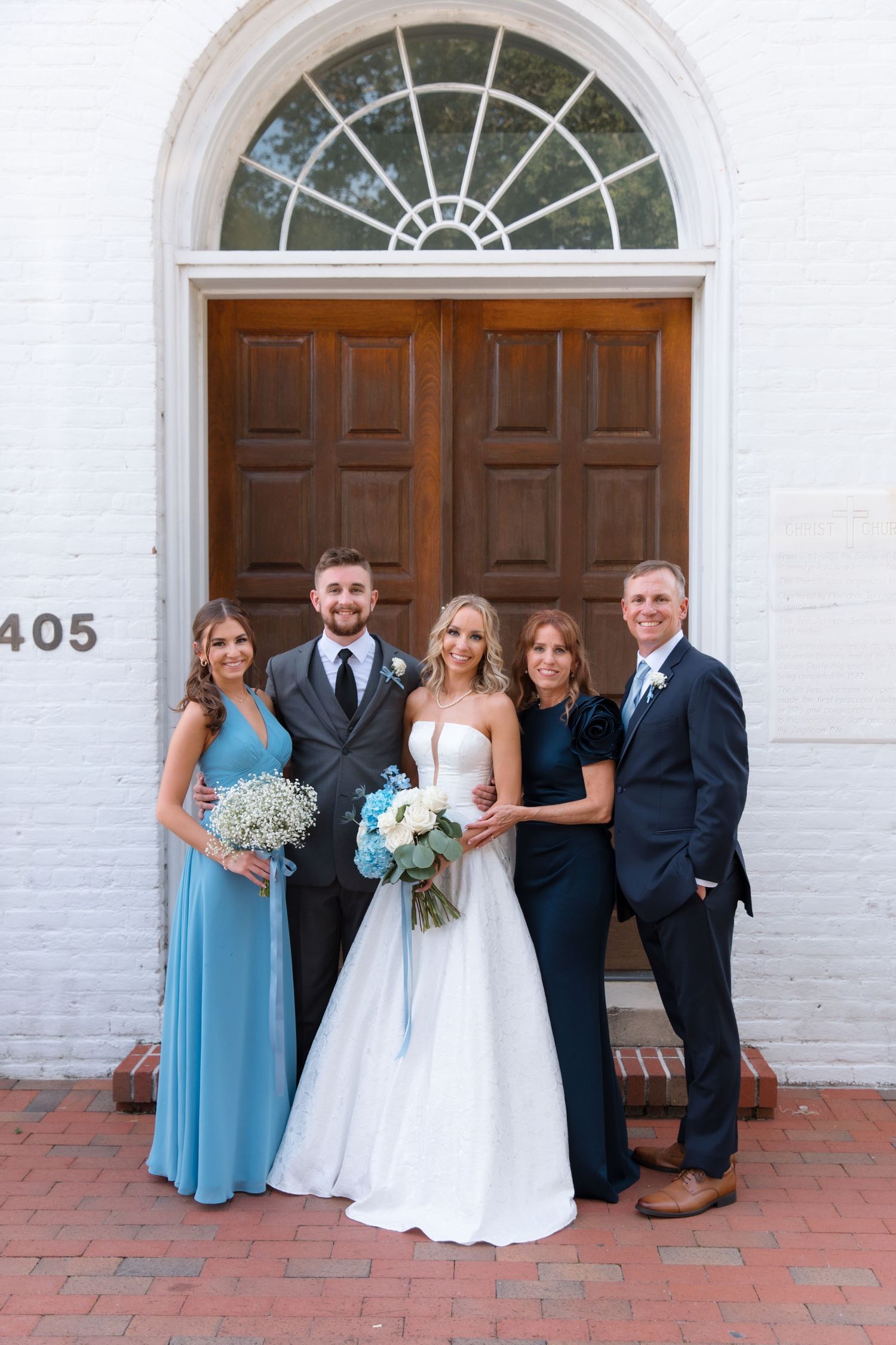 Wedding party in blue and white attire posed in front of historic church entrance.