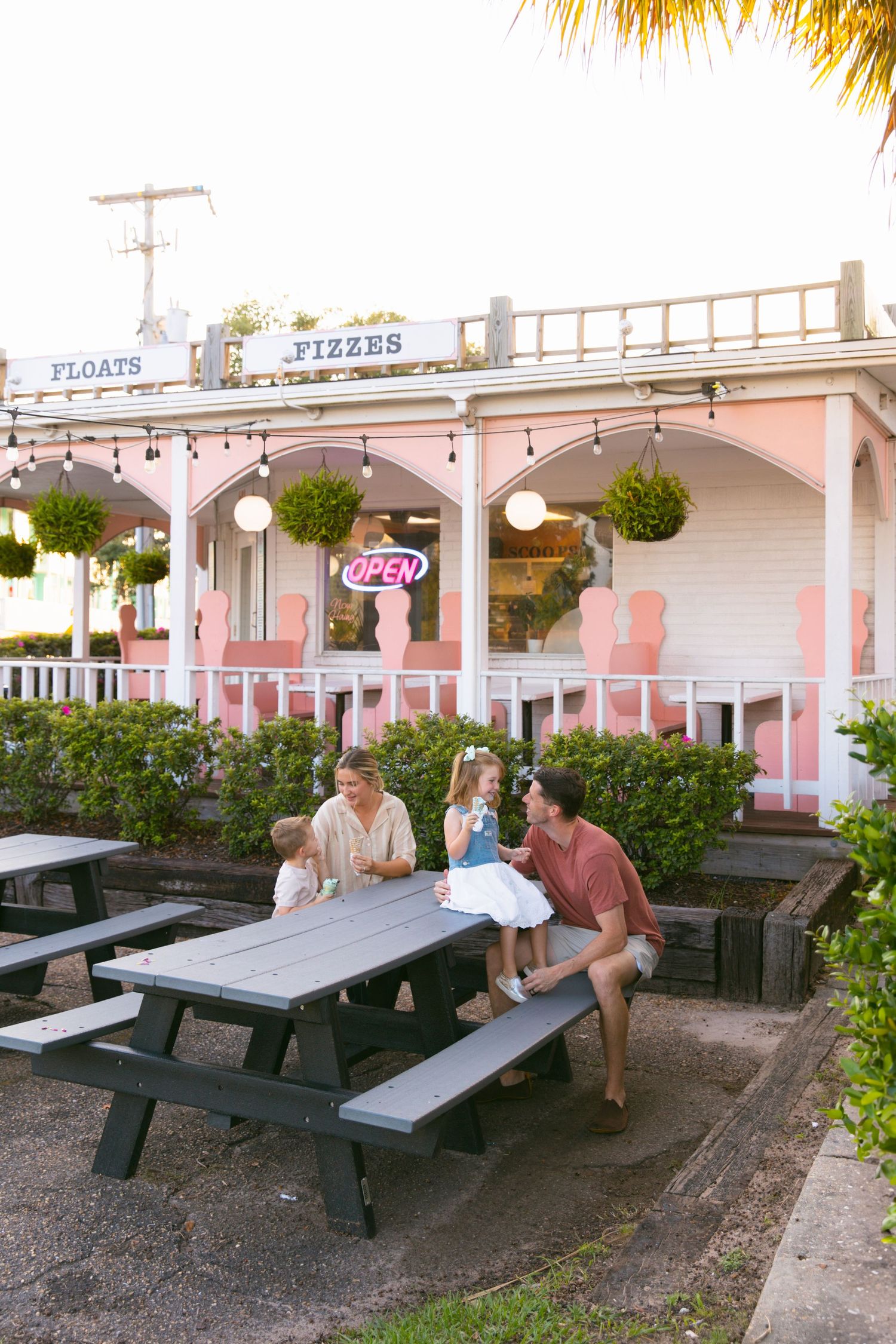 Family enjoying ice cream at a pink-themed outdoor restaurant with string lights.