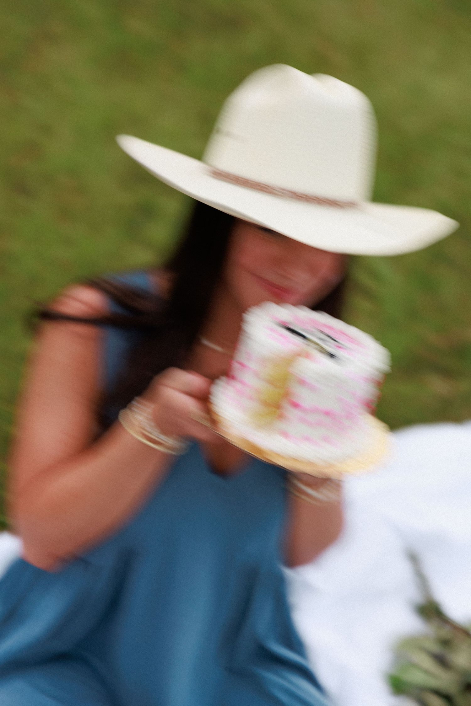 Blurred motion shot of someone in blue dress eating cake outdoors.