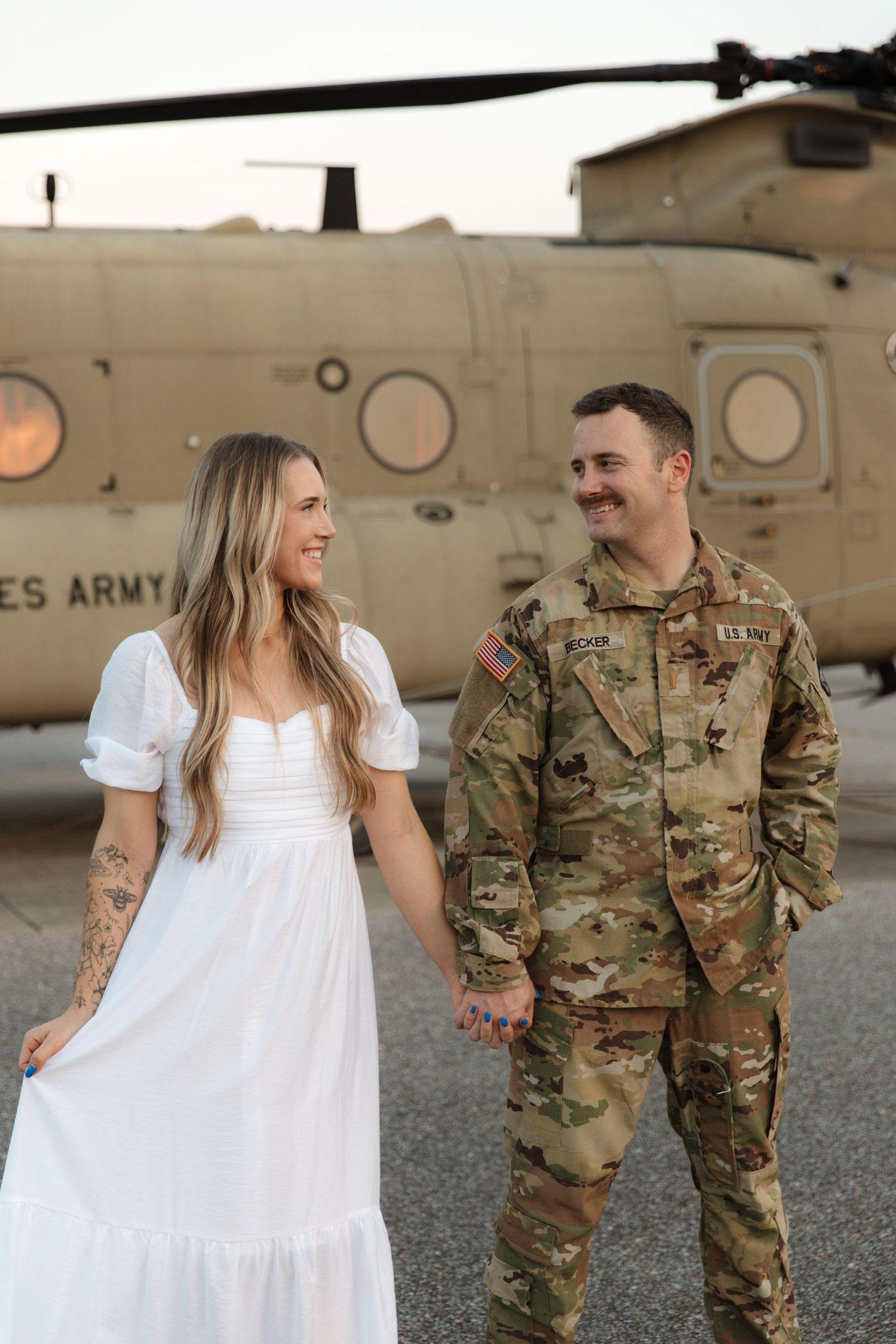 Military couple sharing a happy moment in front of an Army helicopter.