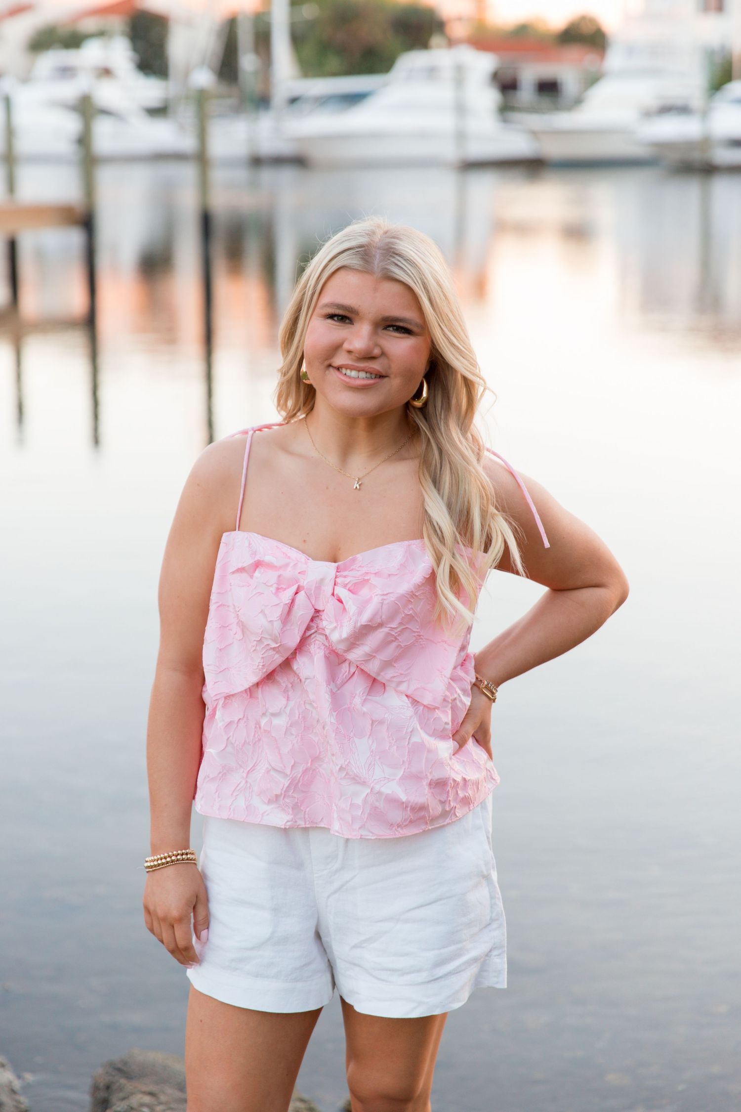 Summer fashion portrait featuring white shorts and pink ruffled top by the waterfront.