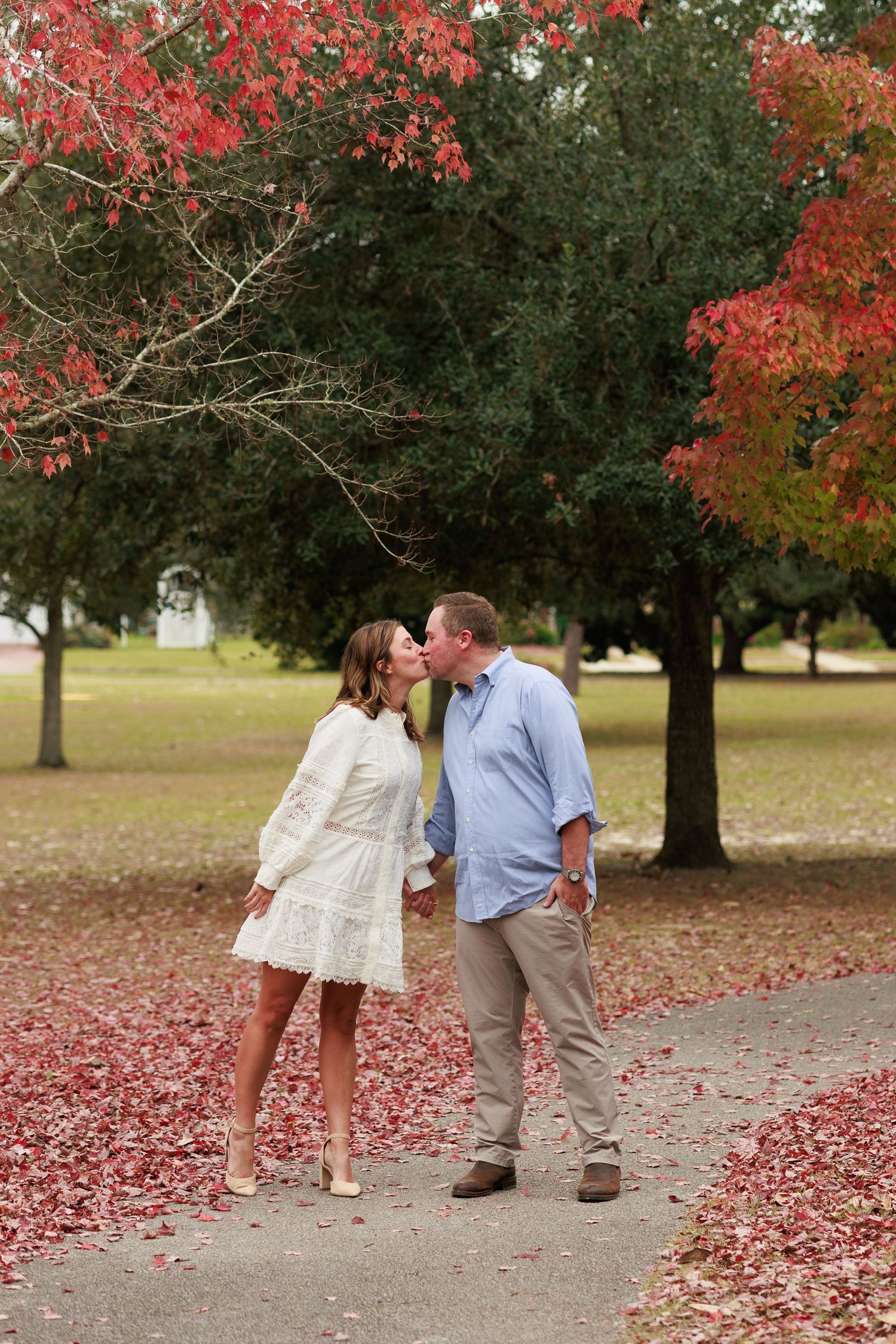 A couple shares a romantic moment on a path surrounded by vibrant red and orange fall foliage.