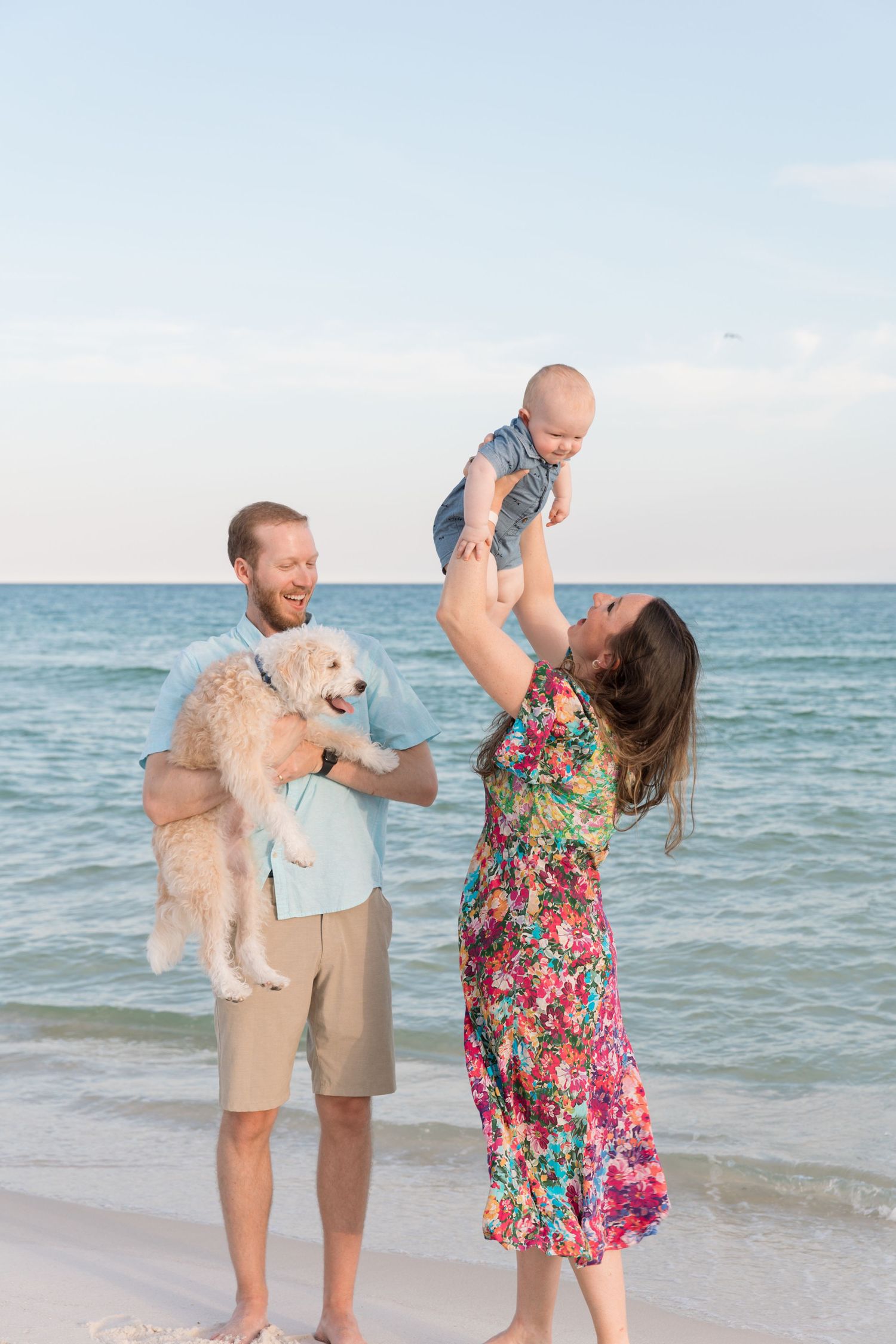 Family and their white dog playing together on a sunny beach with turquoise ocean waters.
