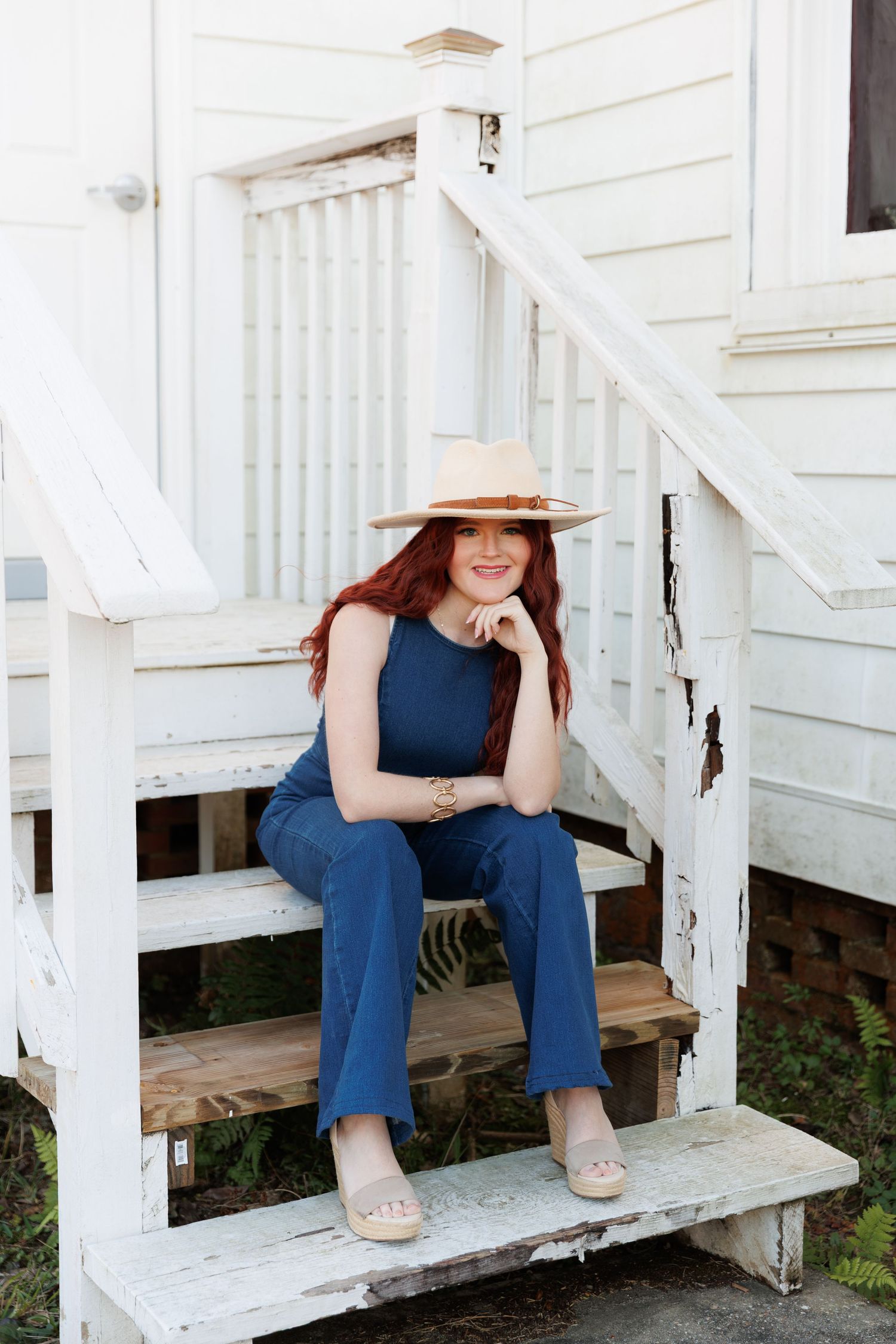 A figure sits on white wooden stairs wearing jeans and a dark top in a casual pose.