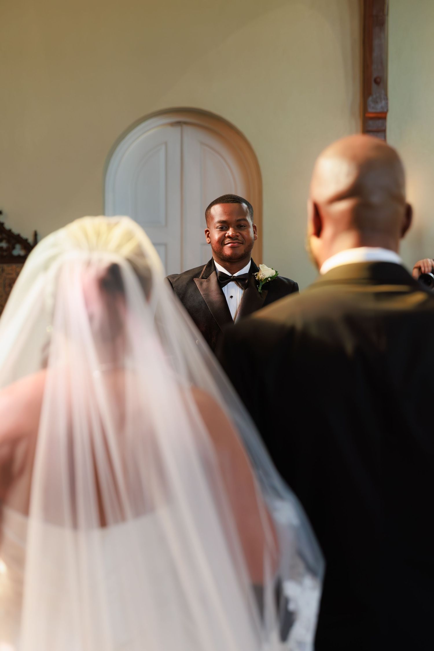 Blurred wedding ceremony scene showing attendees and a white veil in the foreground.