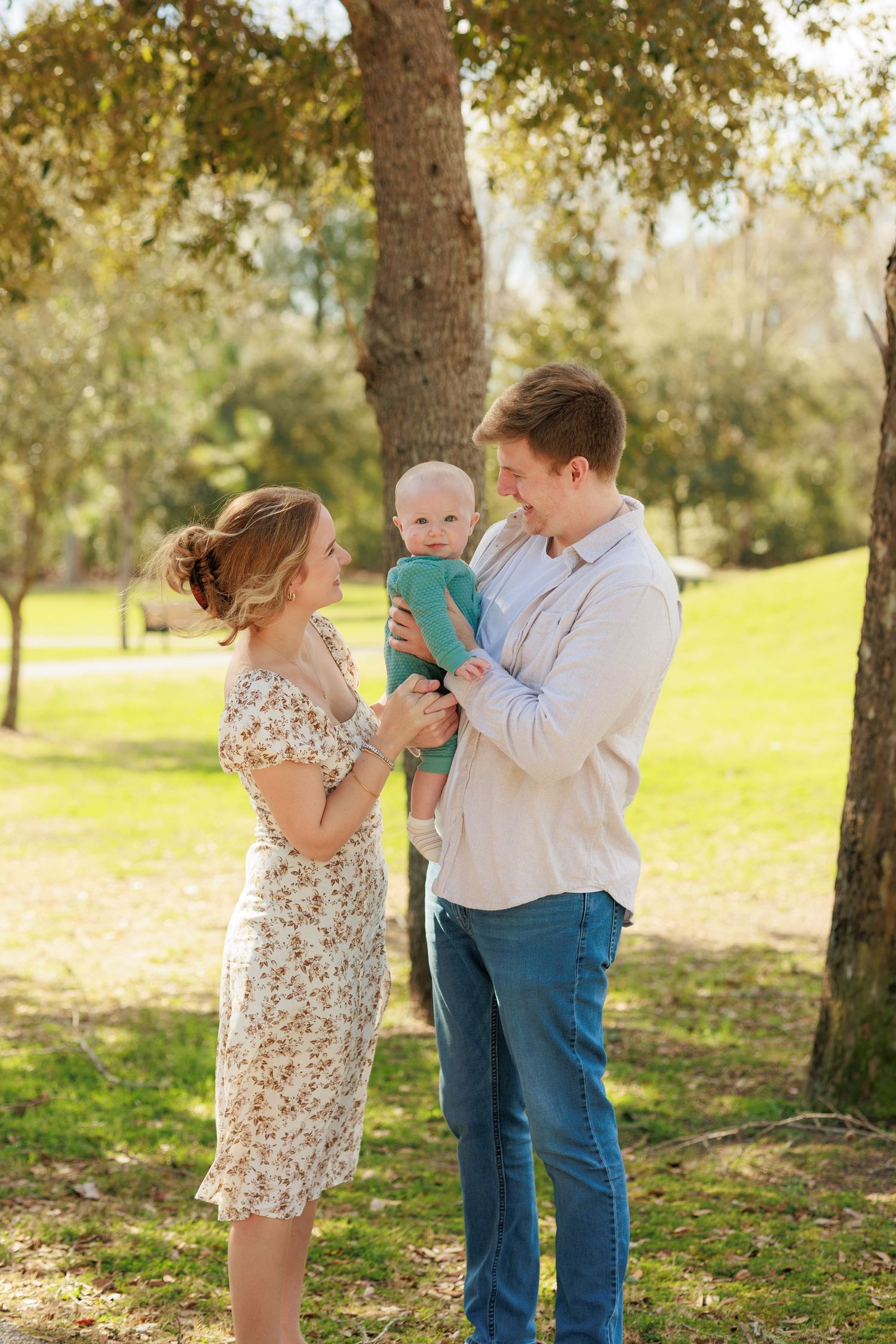 A family shares playful moments together in a sun-dappled park setting during a photo session.