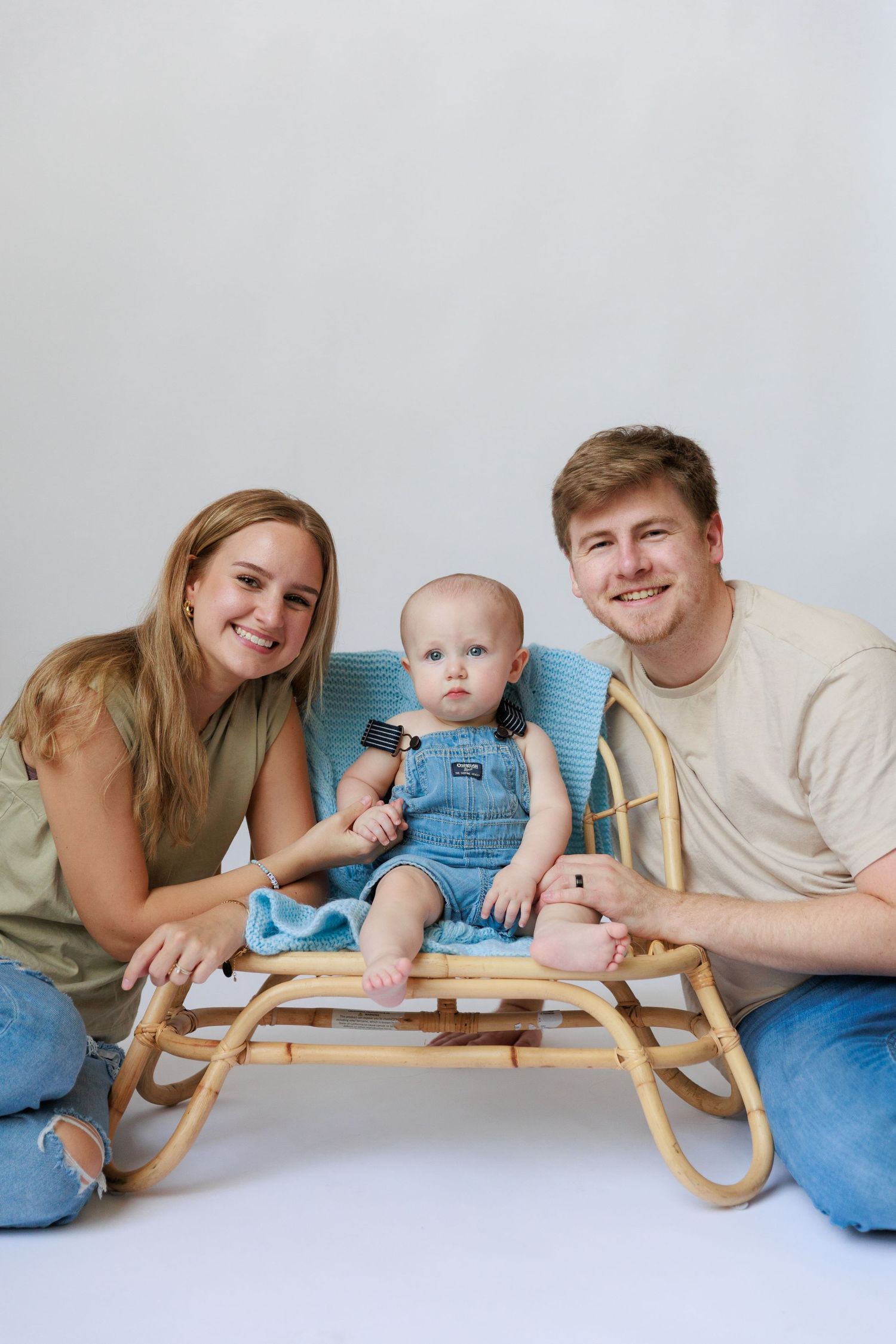 A playful family photo series showing a baby and parents lying on a white floor with a wooden rocking horse.