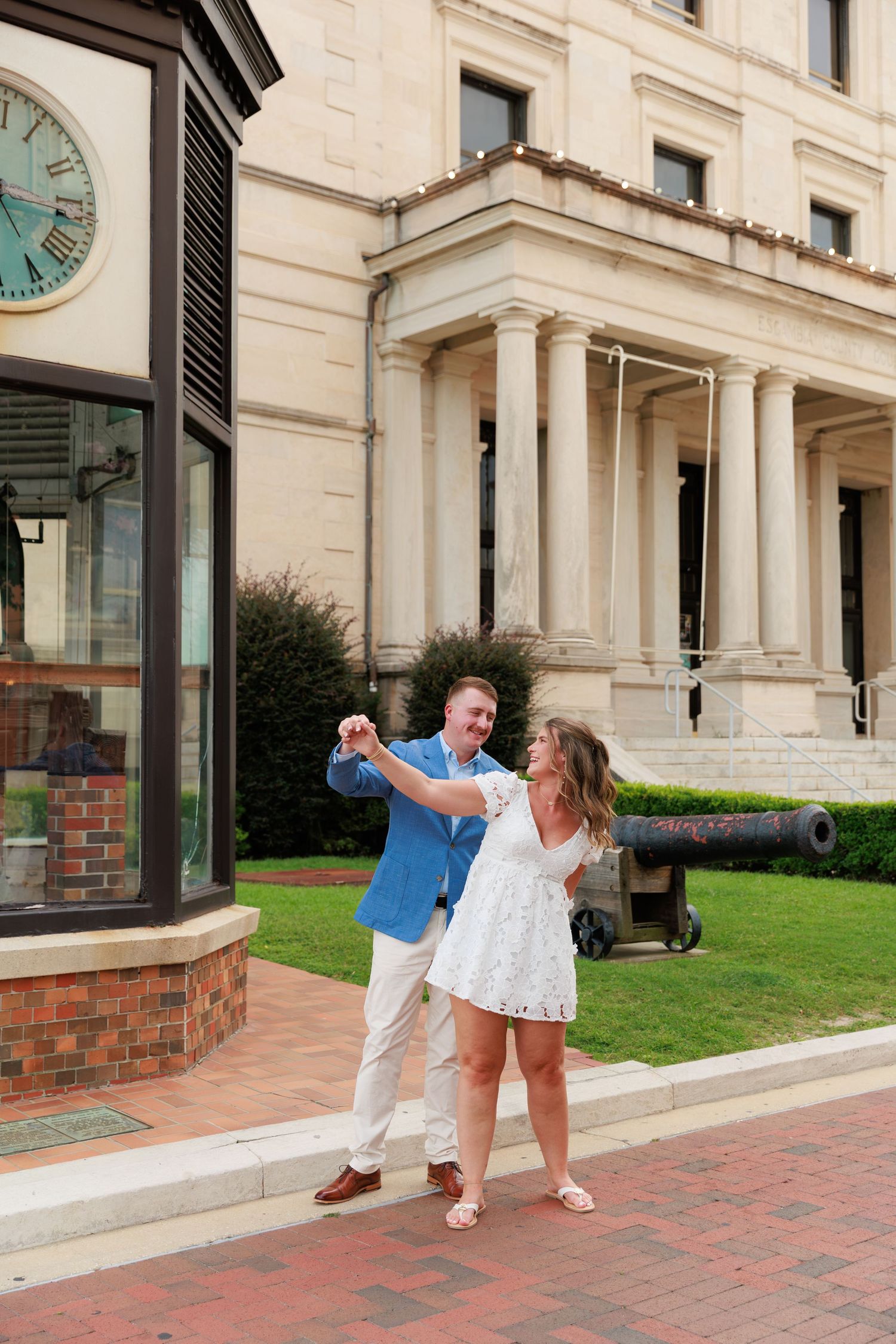 Couple dancing and spinning outside a historic building with columns, man in blue blazer and woman in white dress.