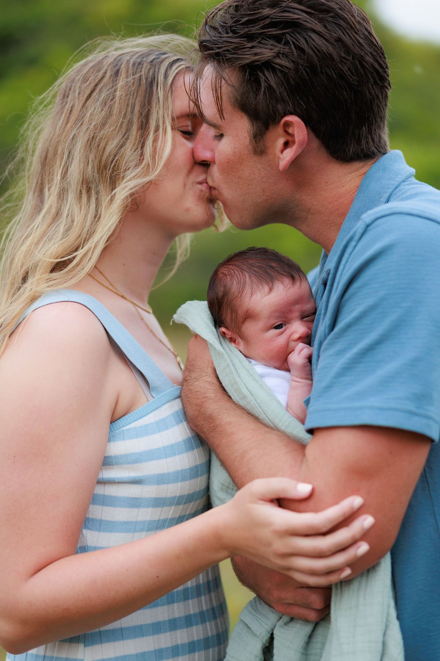 An intimate family portrait outdoors showing tender moments with a newborn baby.