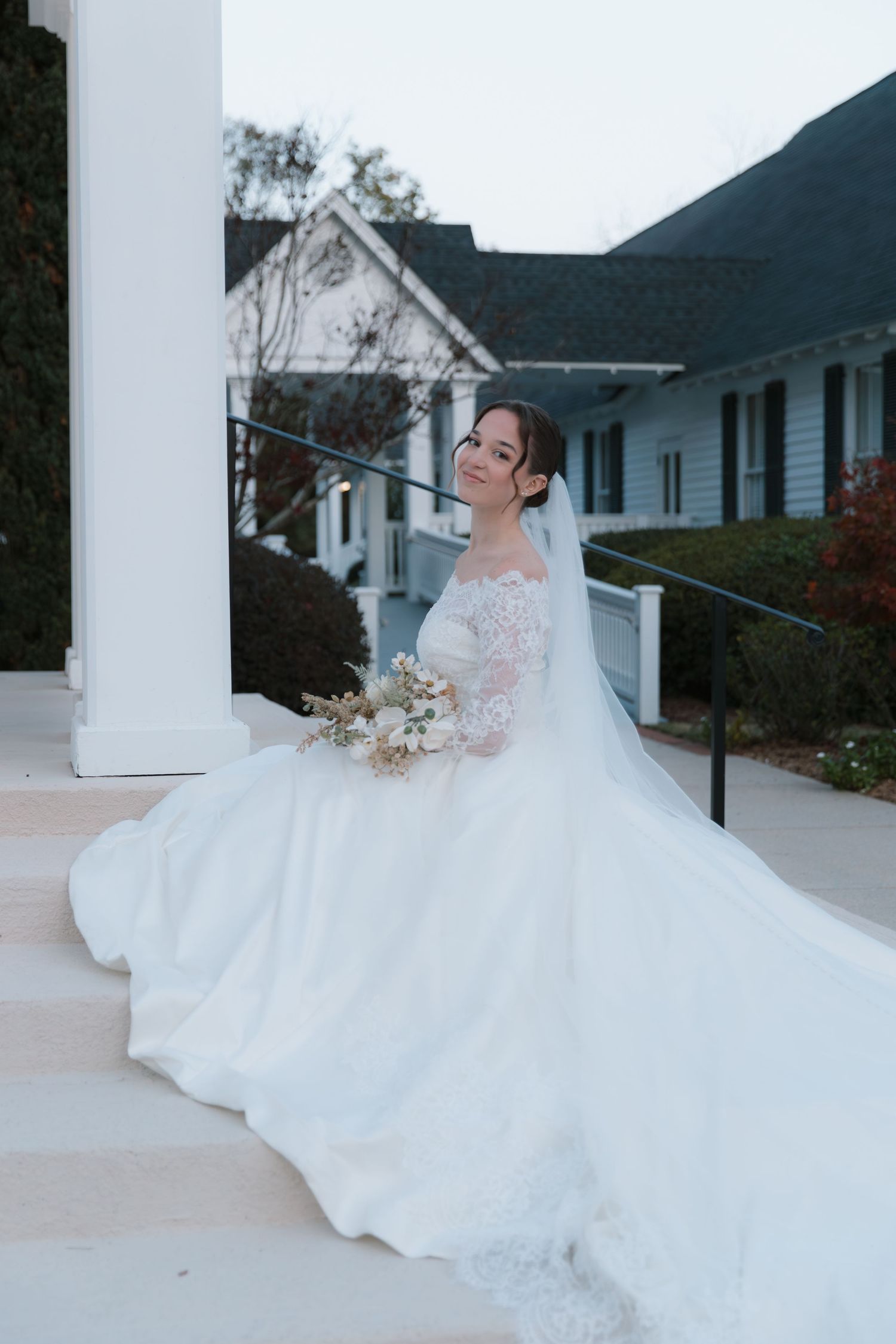 Bride in flowing white gown poses gracefully on church steps with dramatic train spread out.