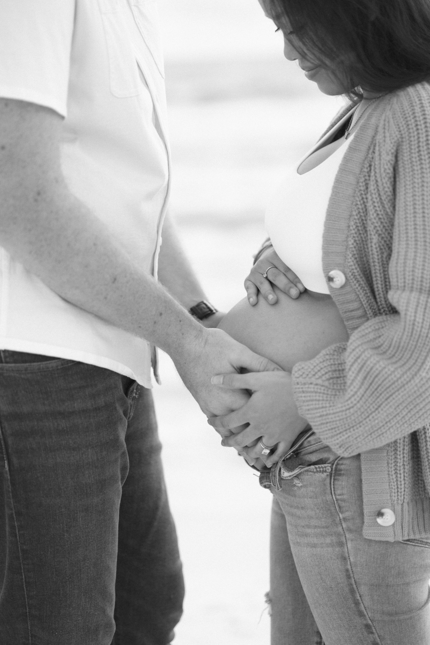 Black and white intimate maternity photos showing close-up shots of couple's hands on pregnant belly.