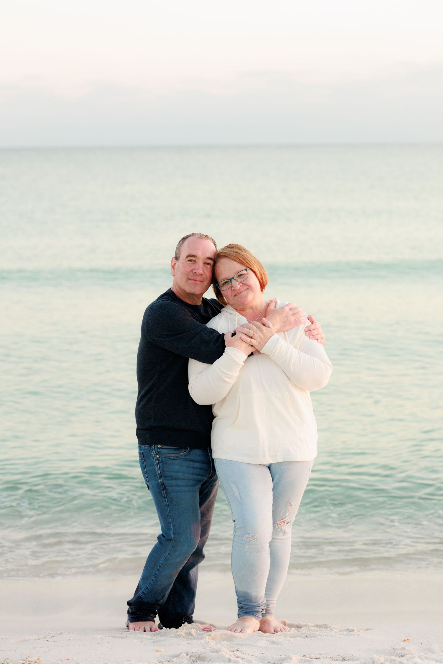 Romantic couple embracing and dancing together on a serene beach with ocean waves in the background.
