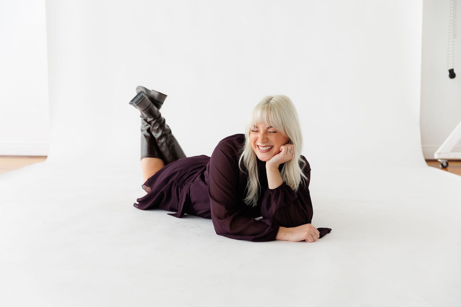 Person in burgundy outfit lies on white floor while smiling and posing during photo session.