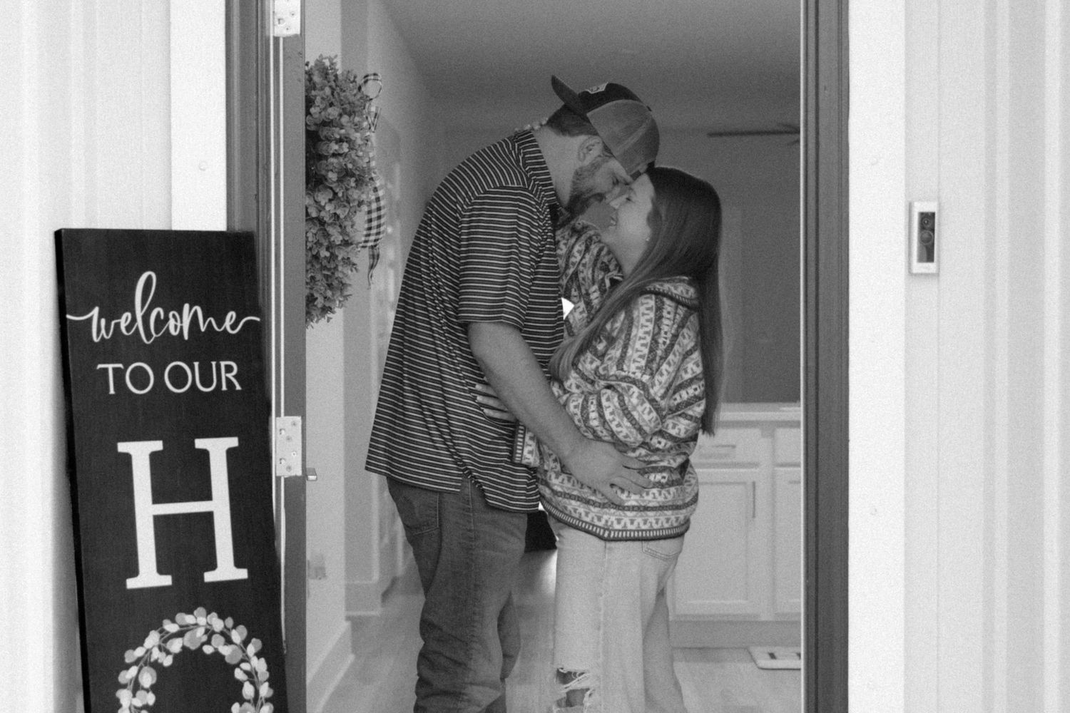 Black and white photo of a tender moment shared in a doorway with a welcome sign visible.