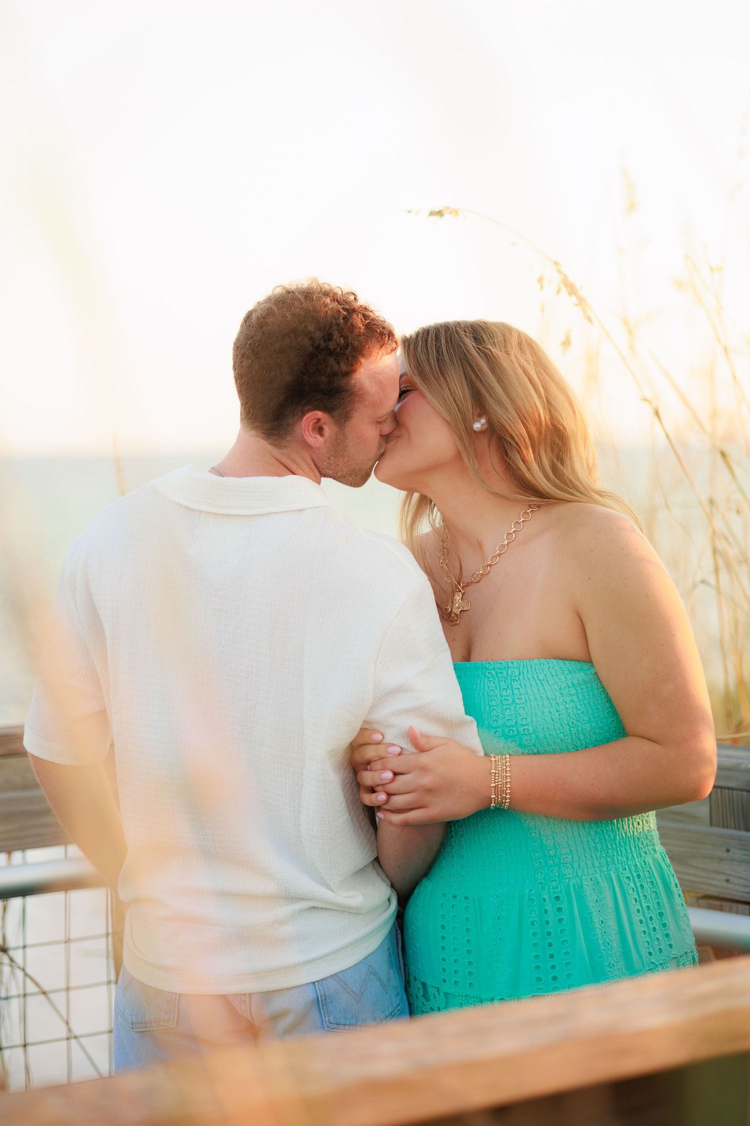 Intimate beach photoshoot with couple in turquoise dress and white shirt against golden light.