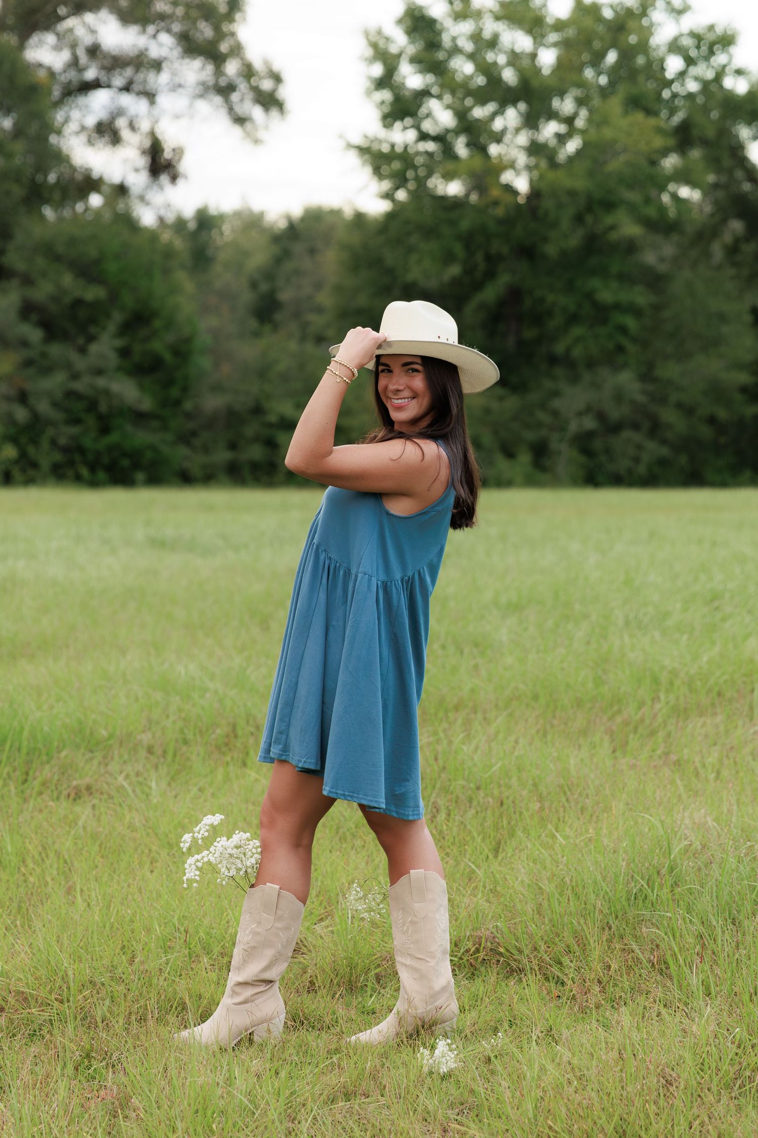 Stylish country fashion look featuring a blue sundress and cream colored boots in an open meadow.
