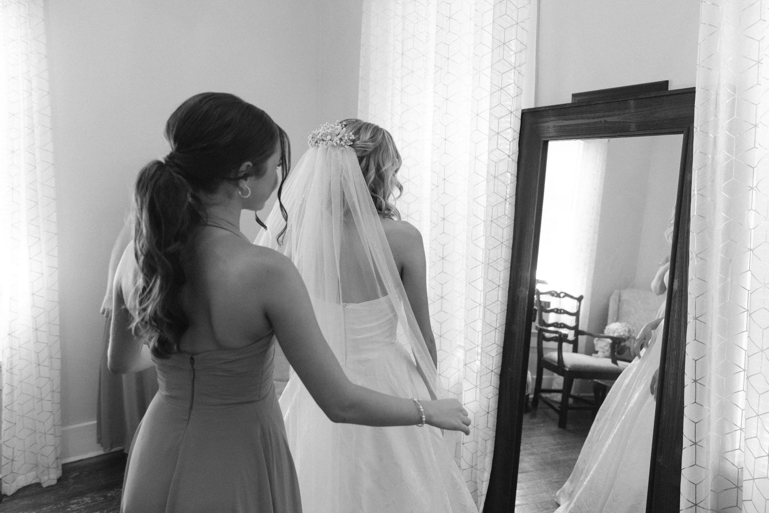 Wedding preparation moment captured in black and white as attendant helps adjust bridal veil.