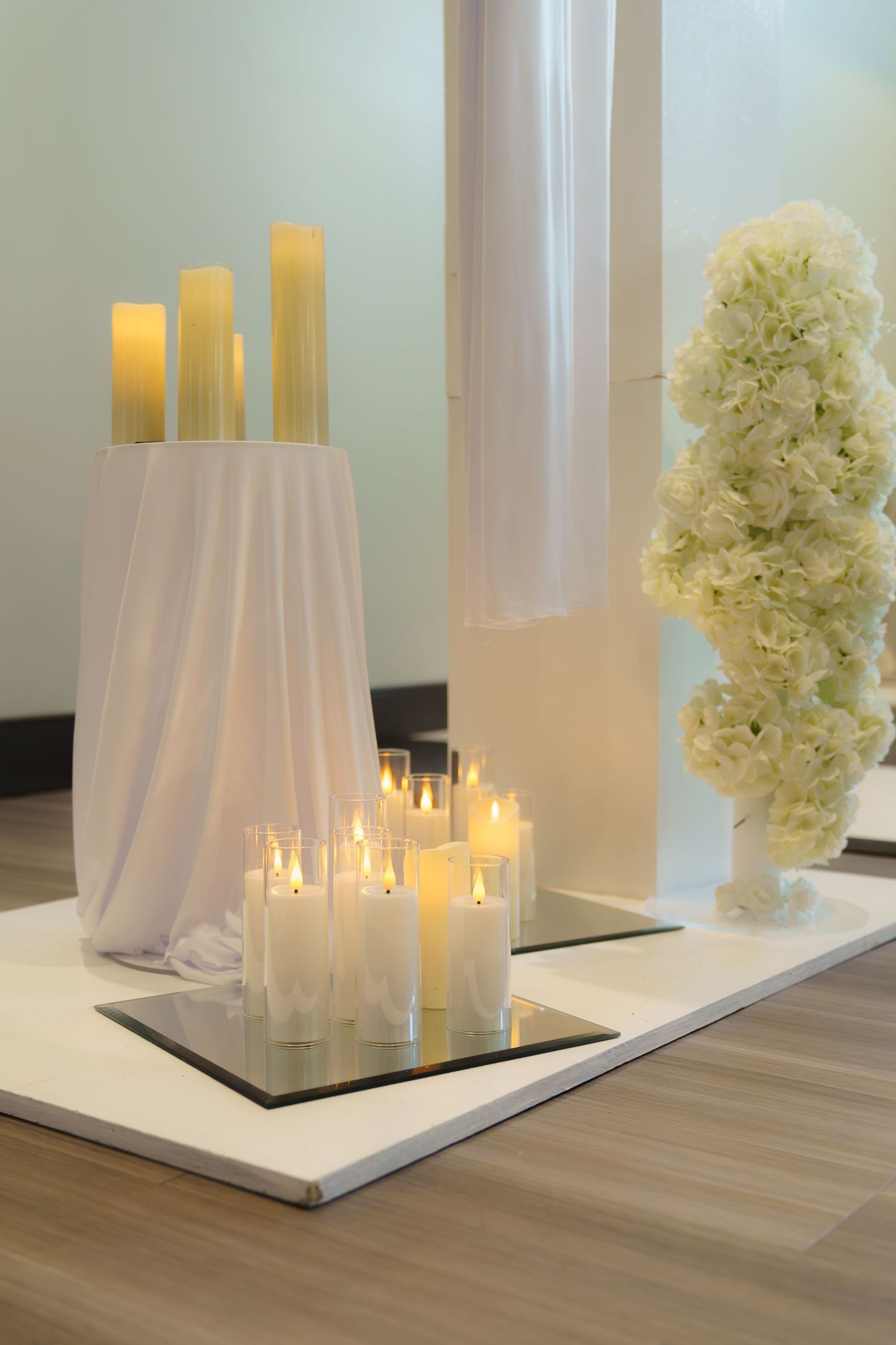 White pillar candles and hydrangea centerpieces create an elegant display on wooden flooring.