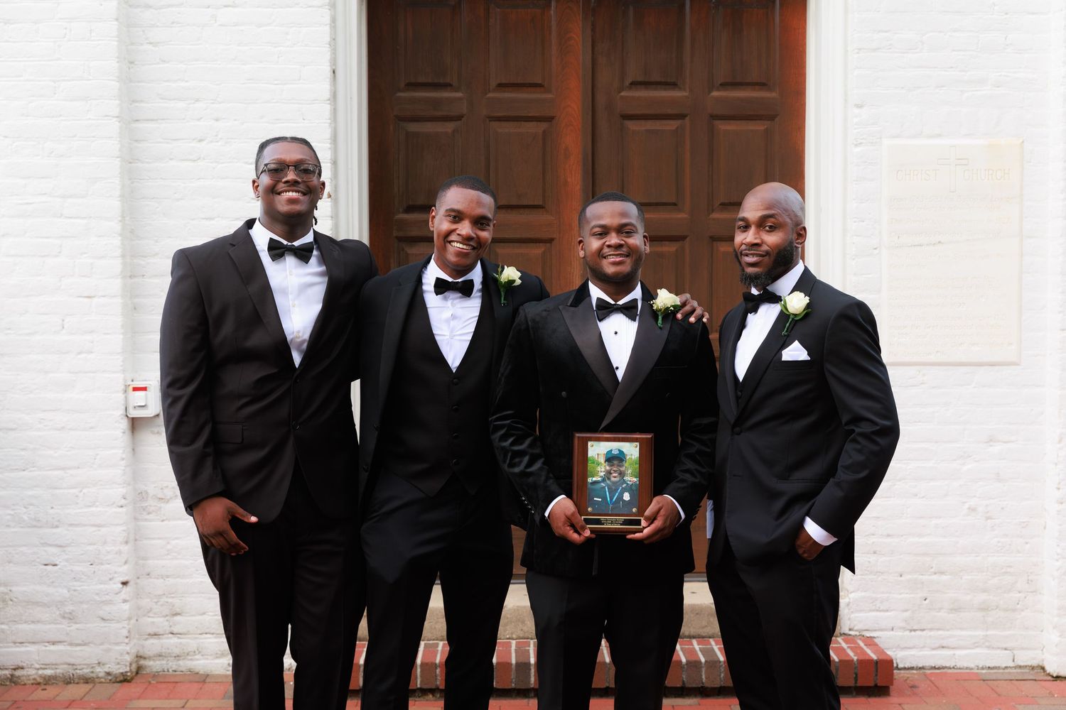 A group of groomsmen in black tuxedos and bow ties pose together for a formal wedding photo.