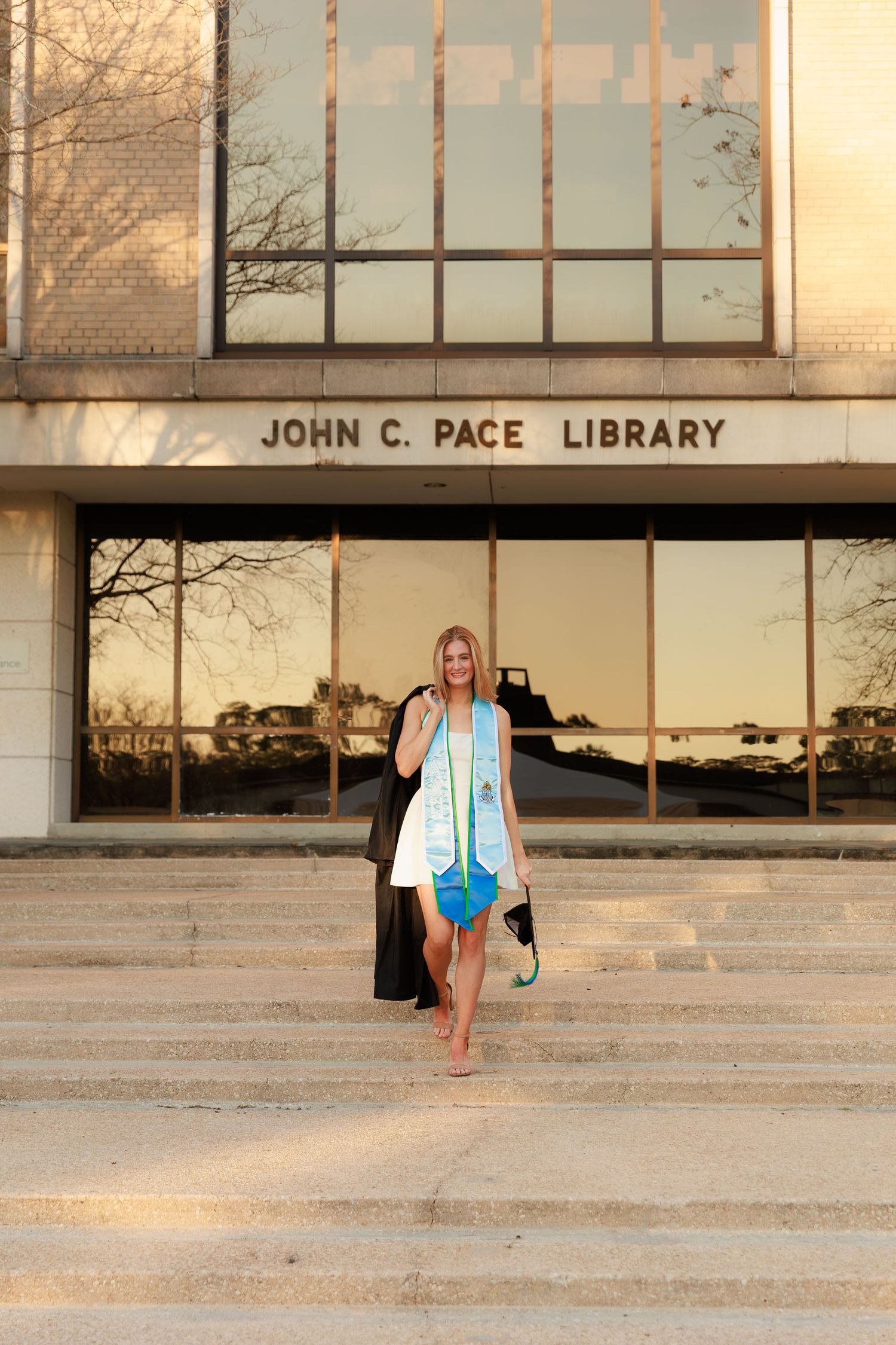 Graduate jumps joyfully on library steps during graduation photo session at John C. Pace Library.