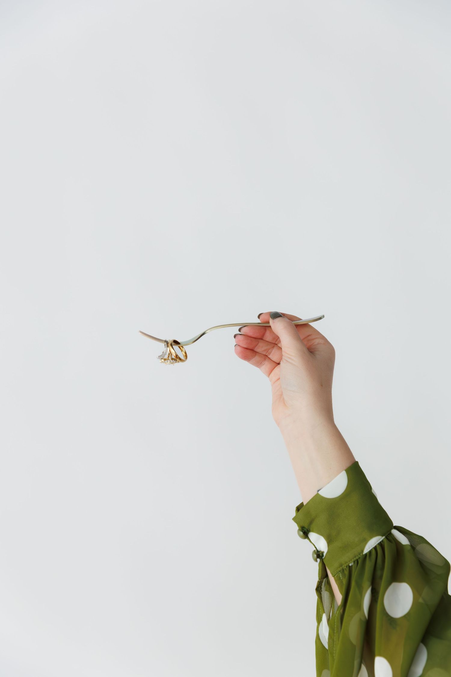 Hands in green polka dot sleeves reach out to photograph a small flying insect against white background.