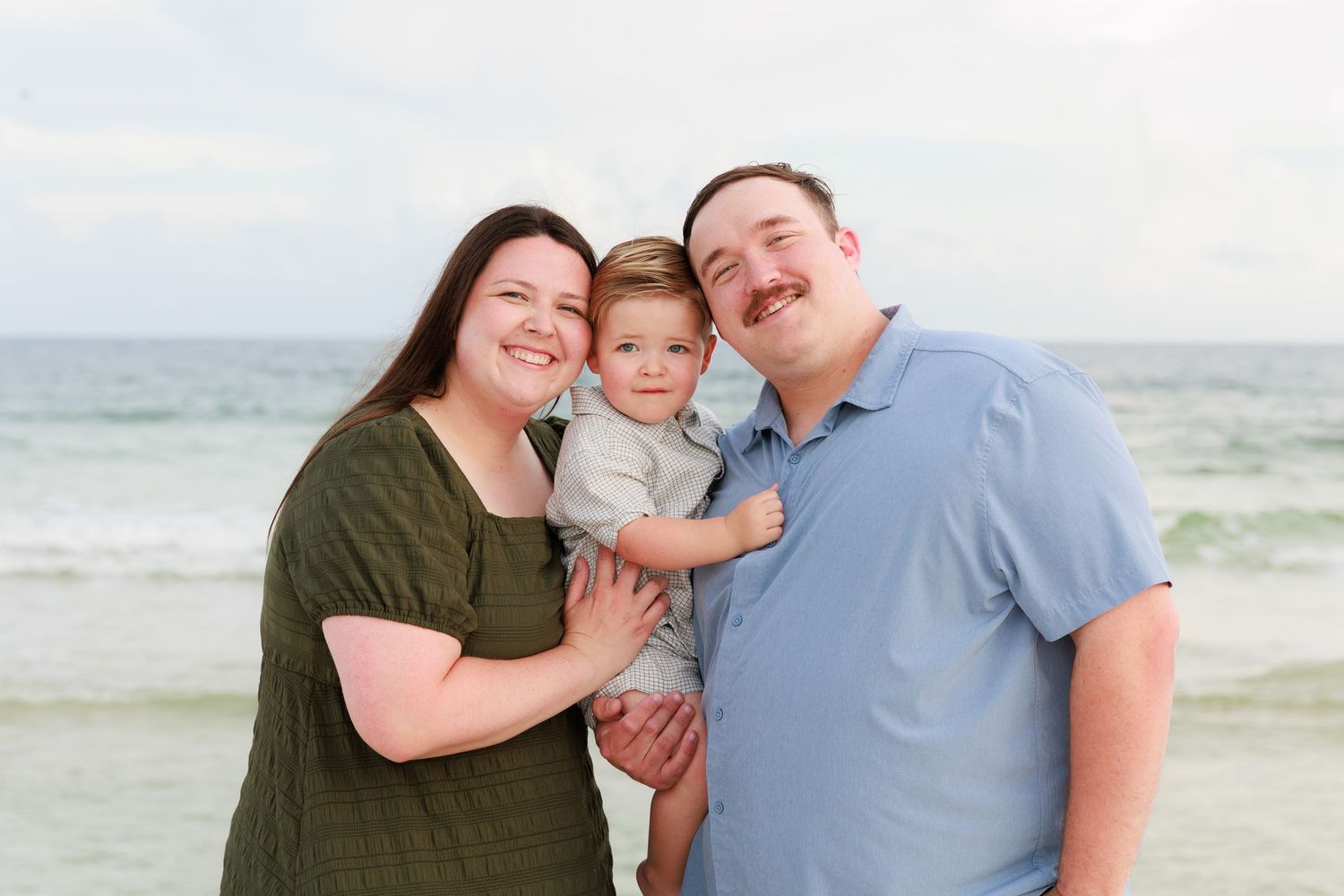 A happy family enjoys a tender moment together on a cloudy beach with ocean waves in the background.