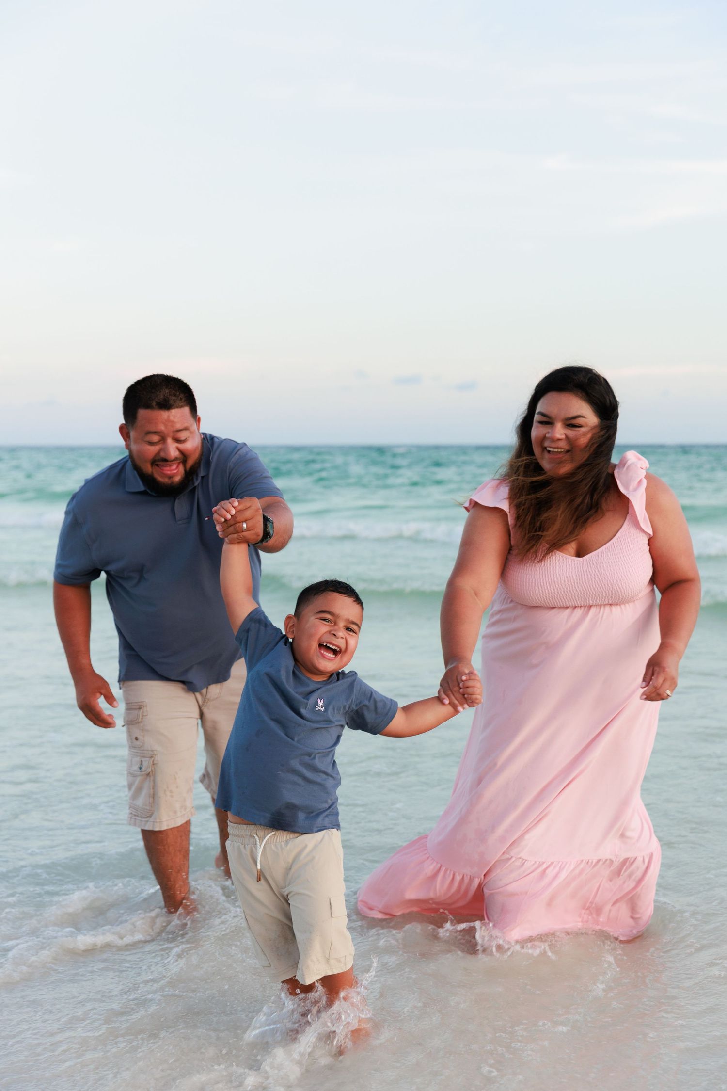 A joyful family plays and splashes in the shallow waters of a beach during sunset.