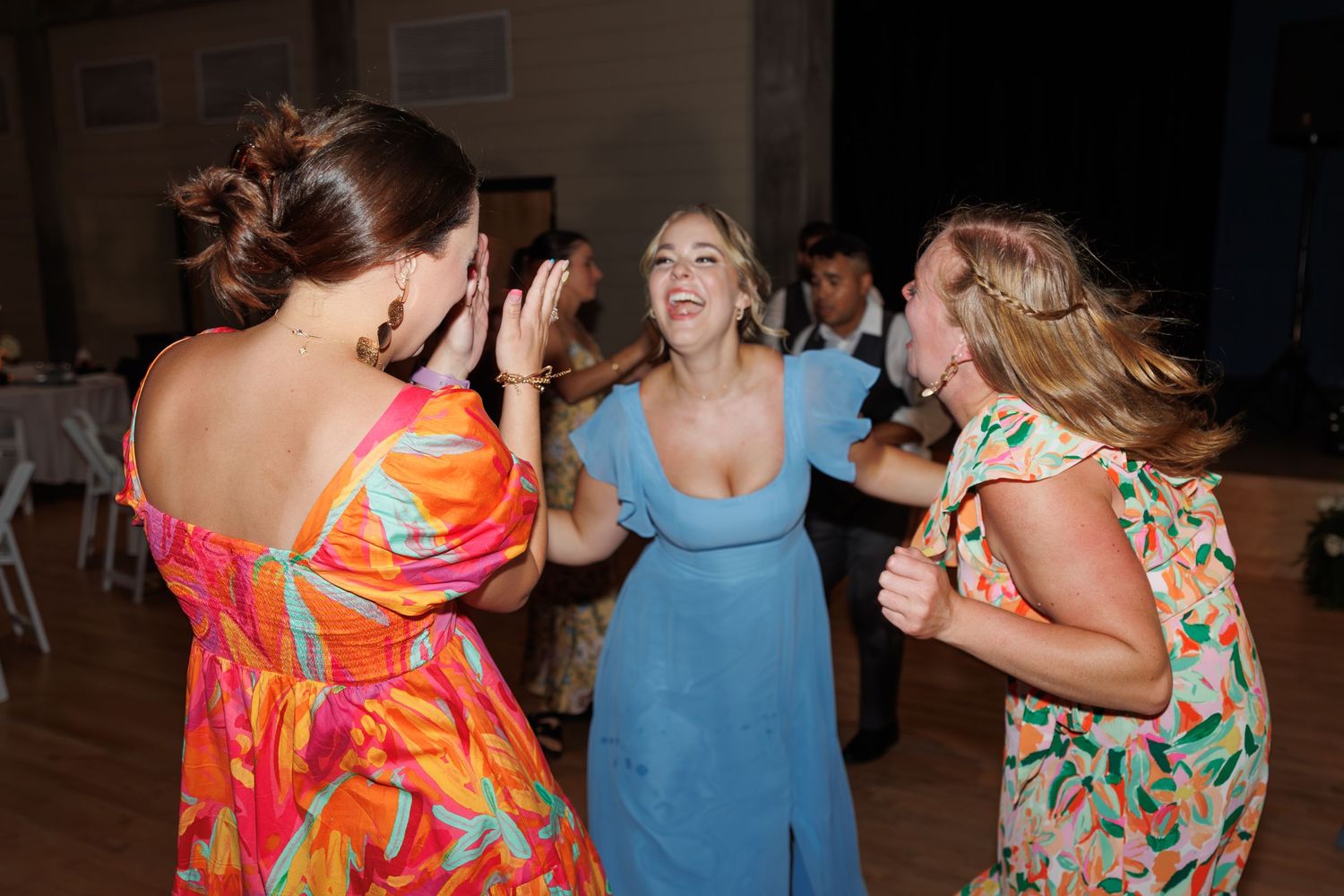 Wedding guests dancing enthusiastically in colorful dresses on the dance floor.