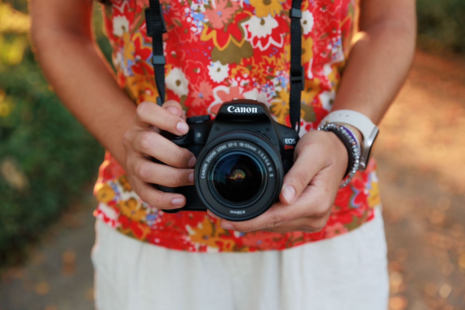 Close-up of hands holding Canon DSLR camera while wearing red floral top.