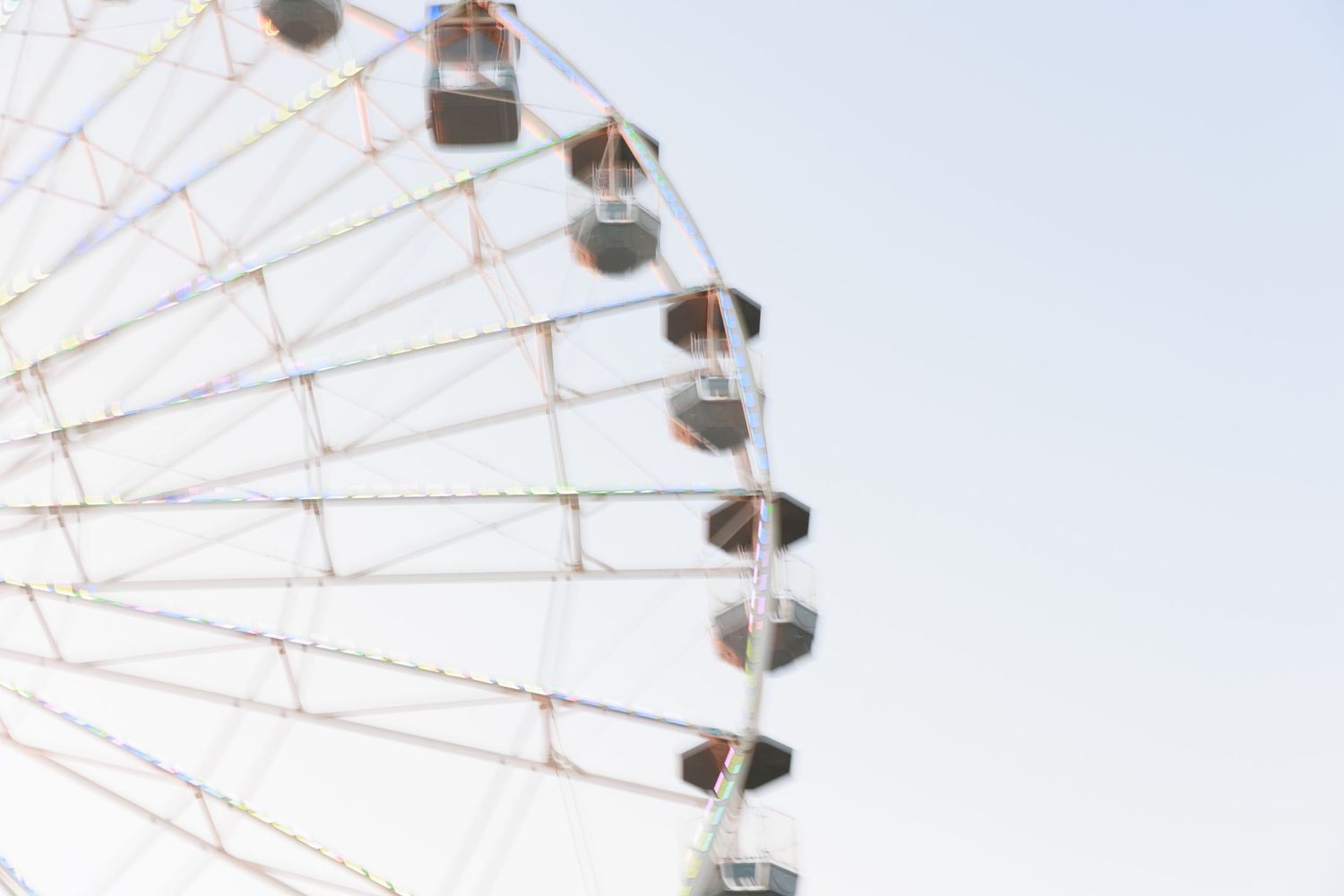 Closeup view of white ferris wheel gondolas against bright blue sky.