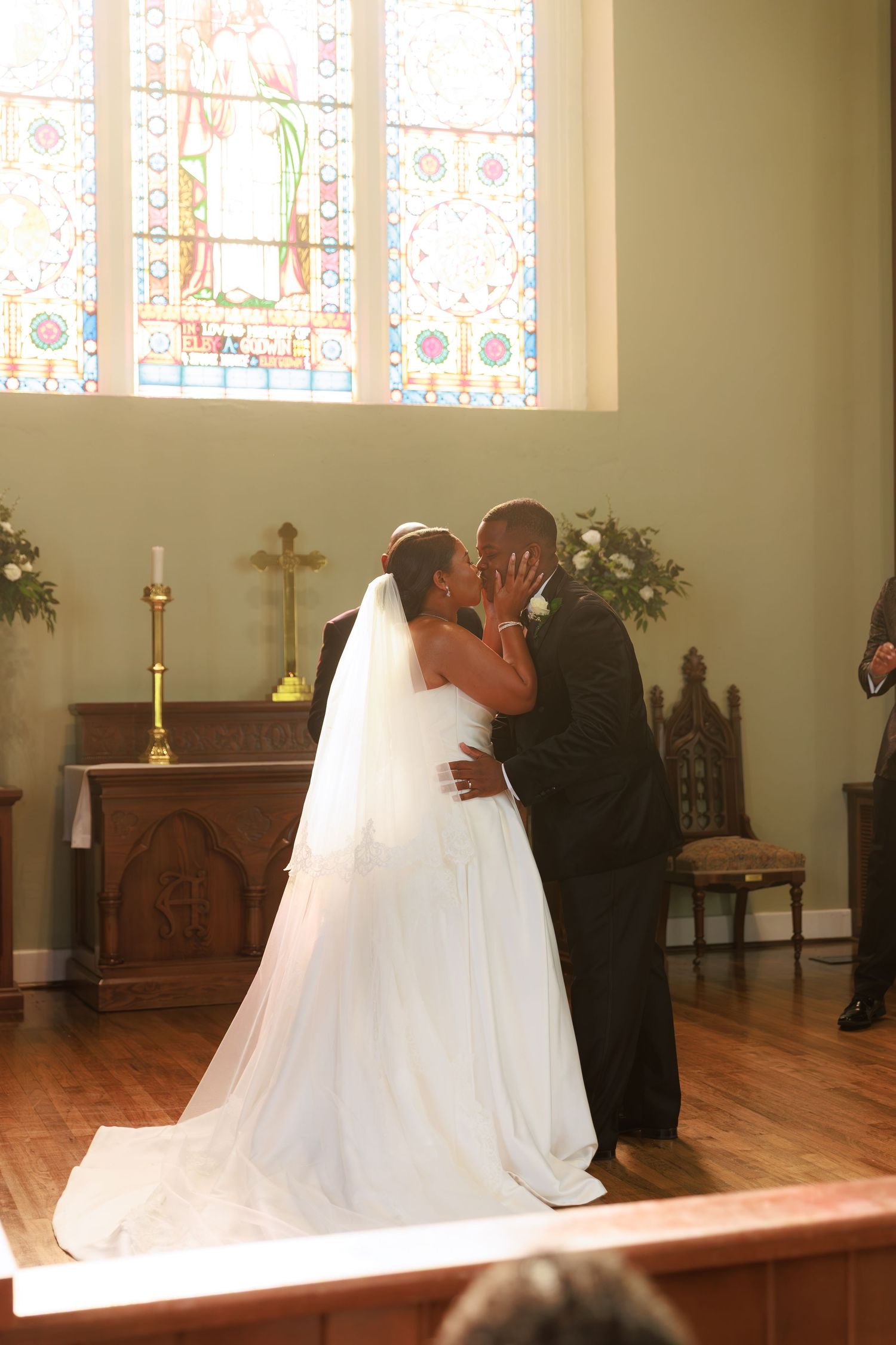A wedding ceremony takes place in a church sanctuary with stained glass windows and wooden pews.