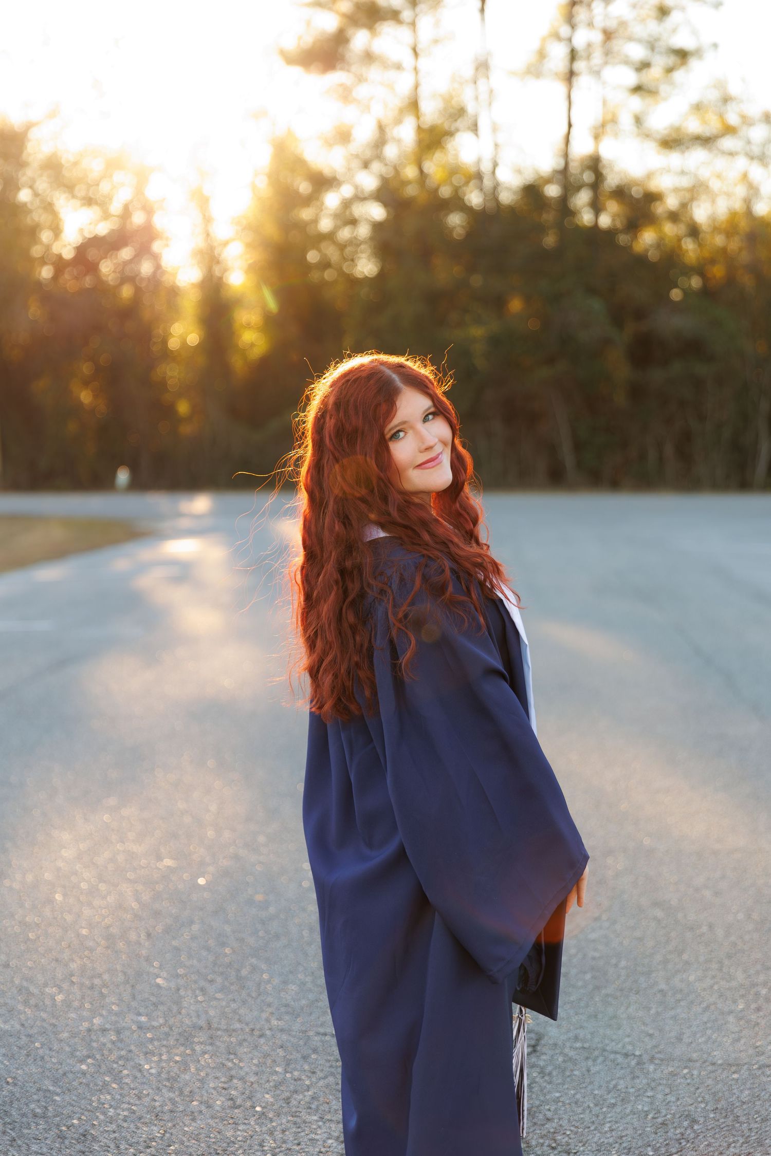Person in navy blue coat standing on snowy ground at sunset with golden light filtering through trees.