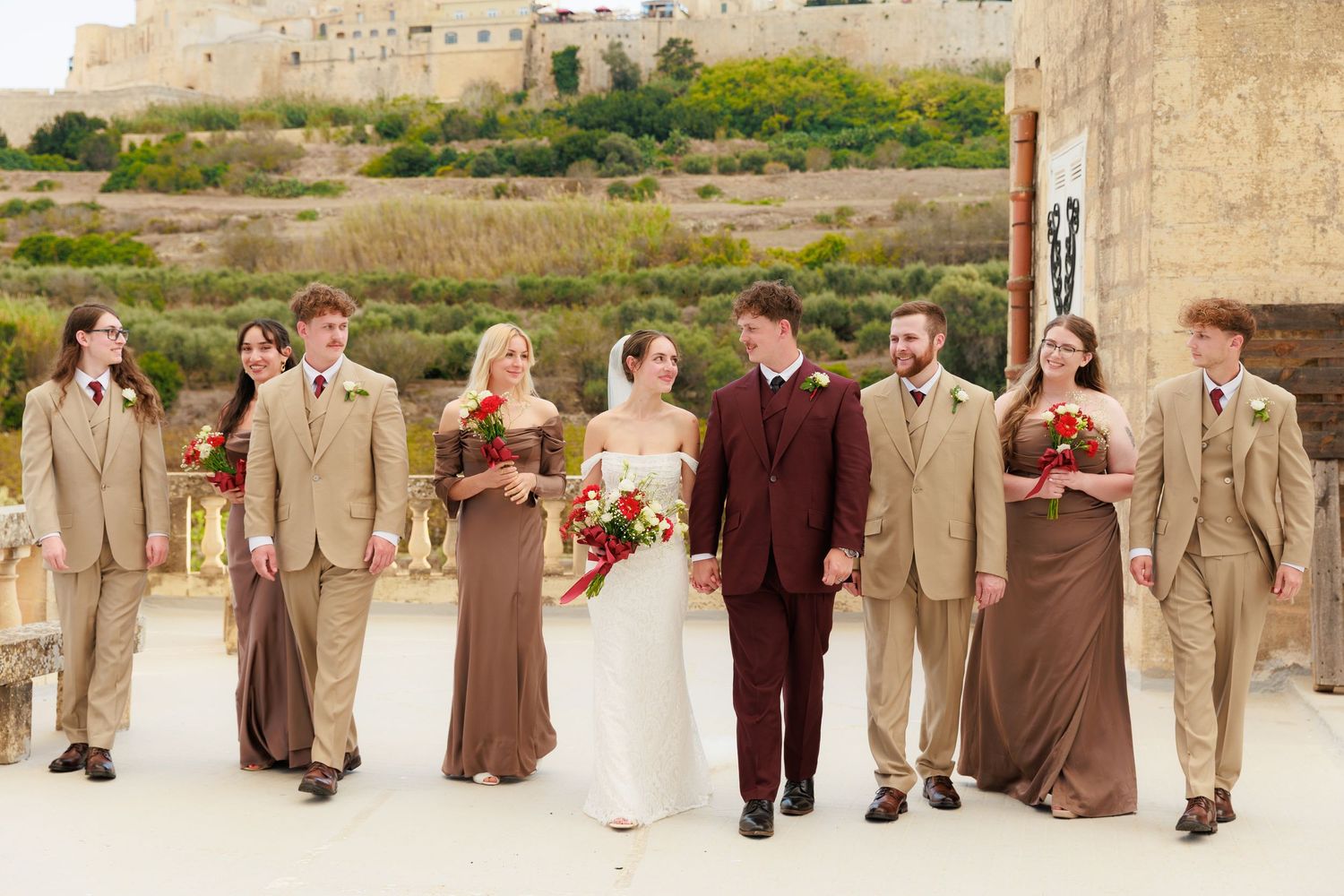 Wedding party walks together along outdoor path wearing coordinated brown and tan formal attire.