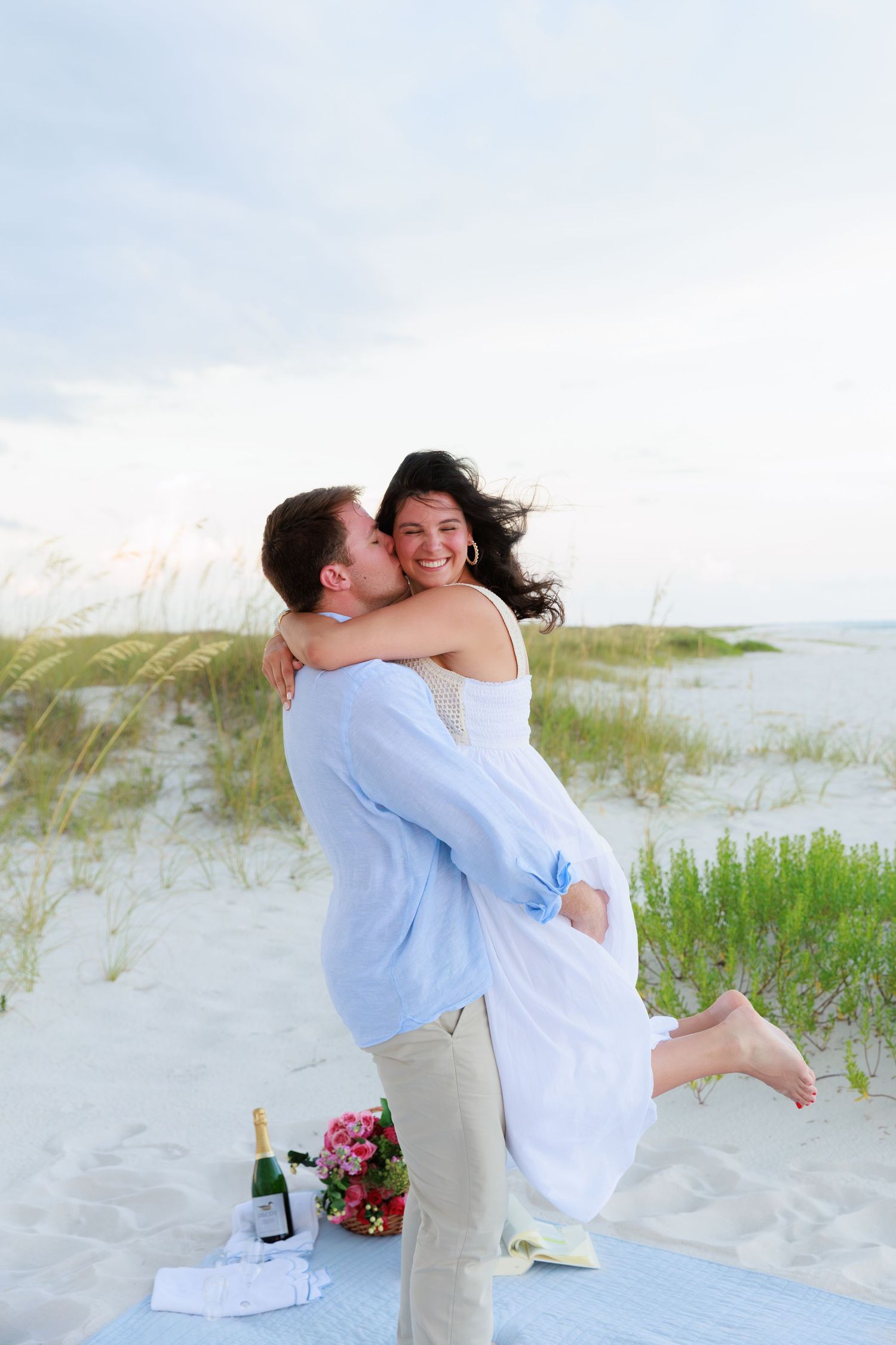 A joyful moment captured on the beach as a couple in coordinating outfits embraces and spins.