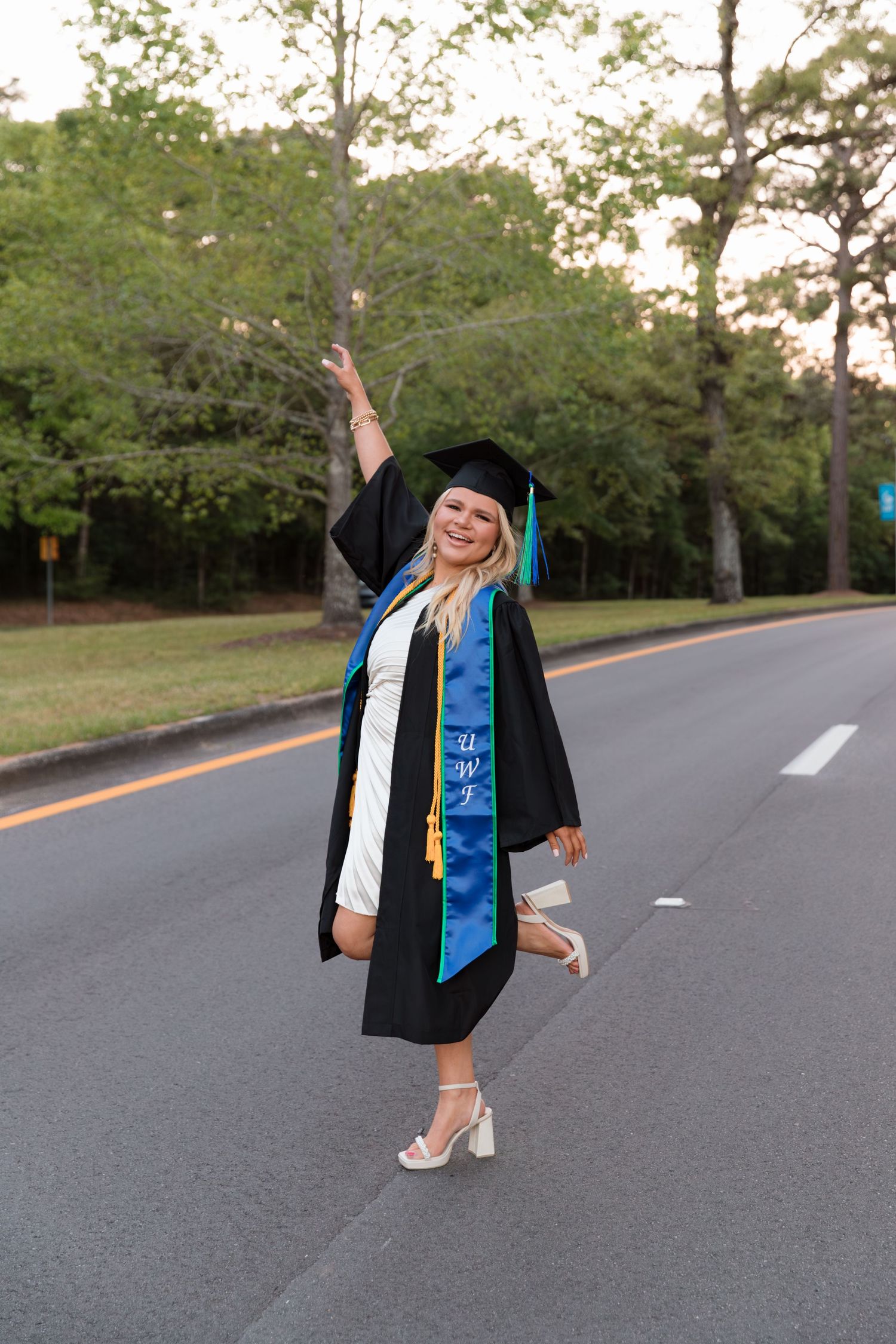 Graduate in cap and gown poses playfully on empty road during outdoor graduation photoshoot.
