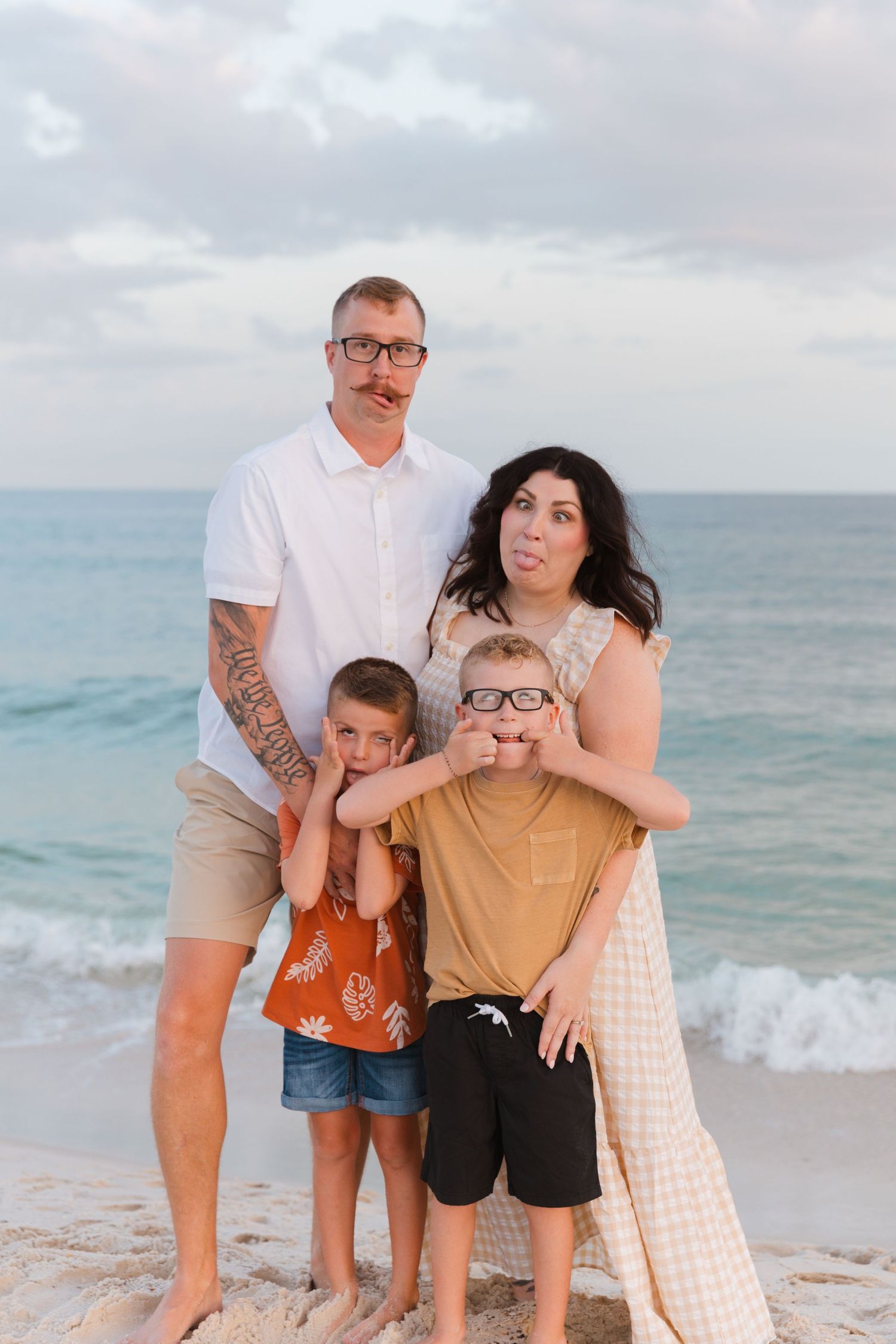 Family portrait on beach with ocean waves and cloudy sky in background.