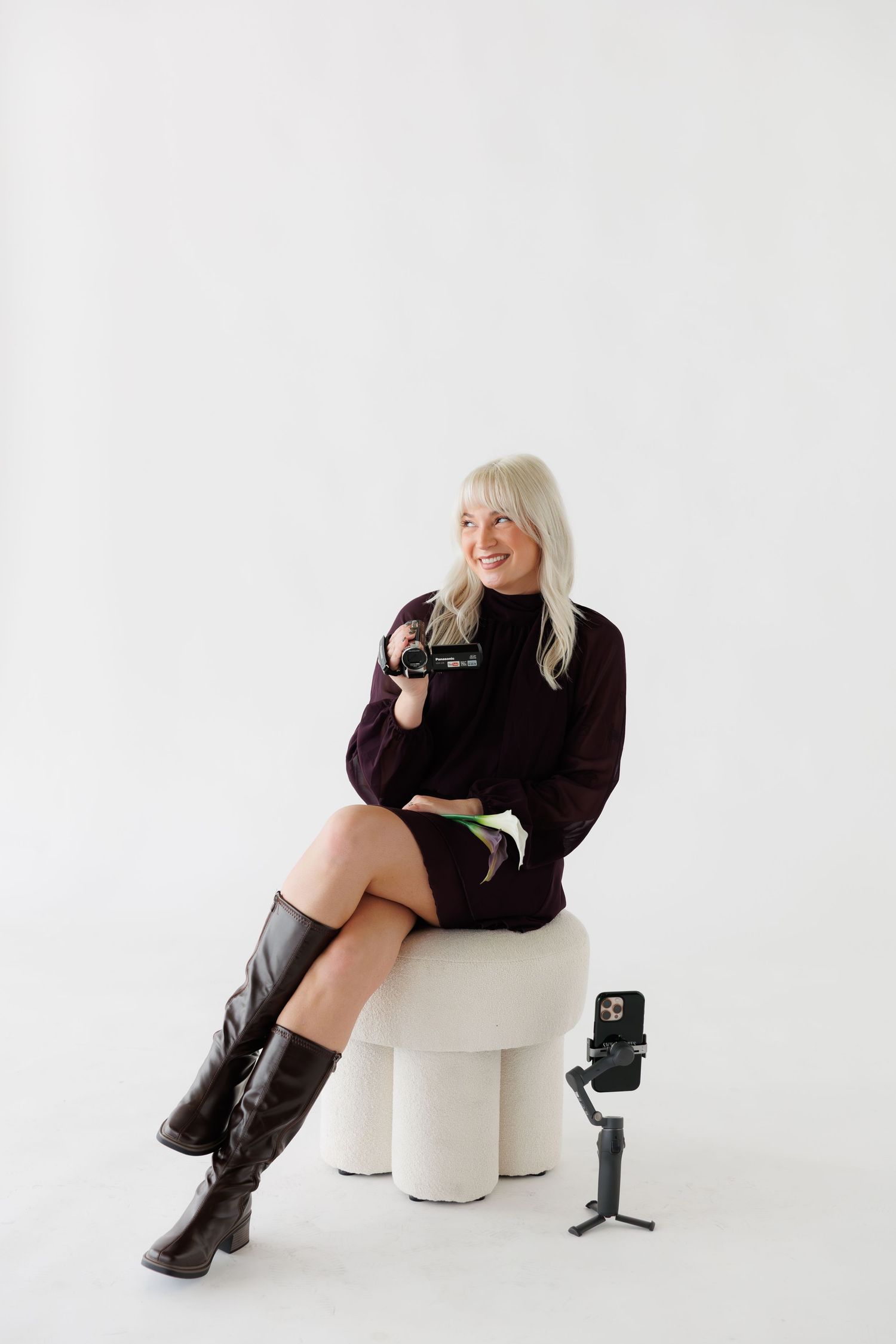 Figure in dark clothing poses casually on white modern furniture with camera equipment nearby.