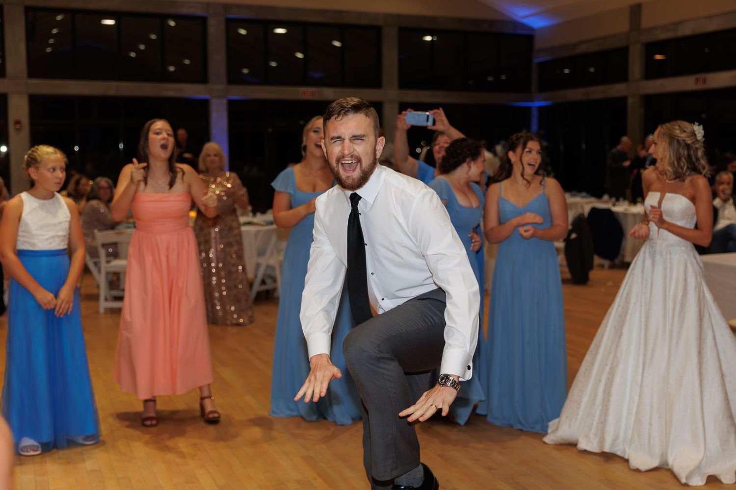 Wedding guest dancing enthusiastically on a wooden dance floor surrounded by bridesmaids.