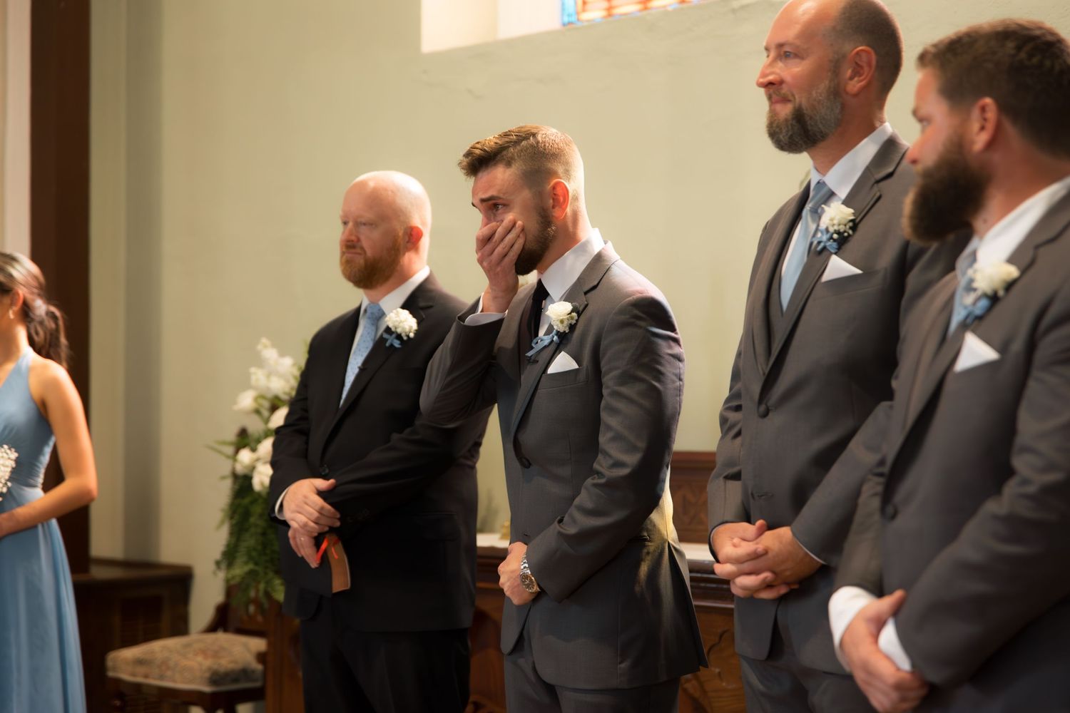 Row of groomsmen in matching gray suits watch ceremony in church.