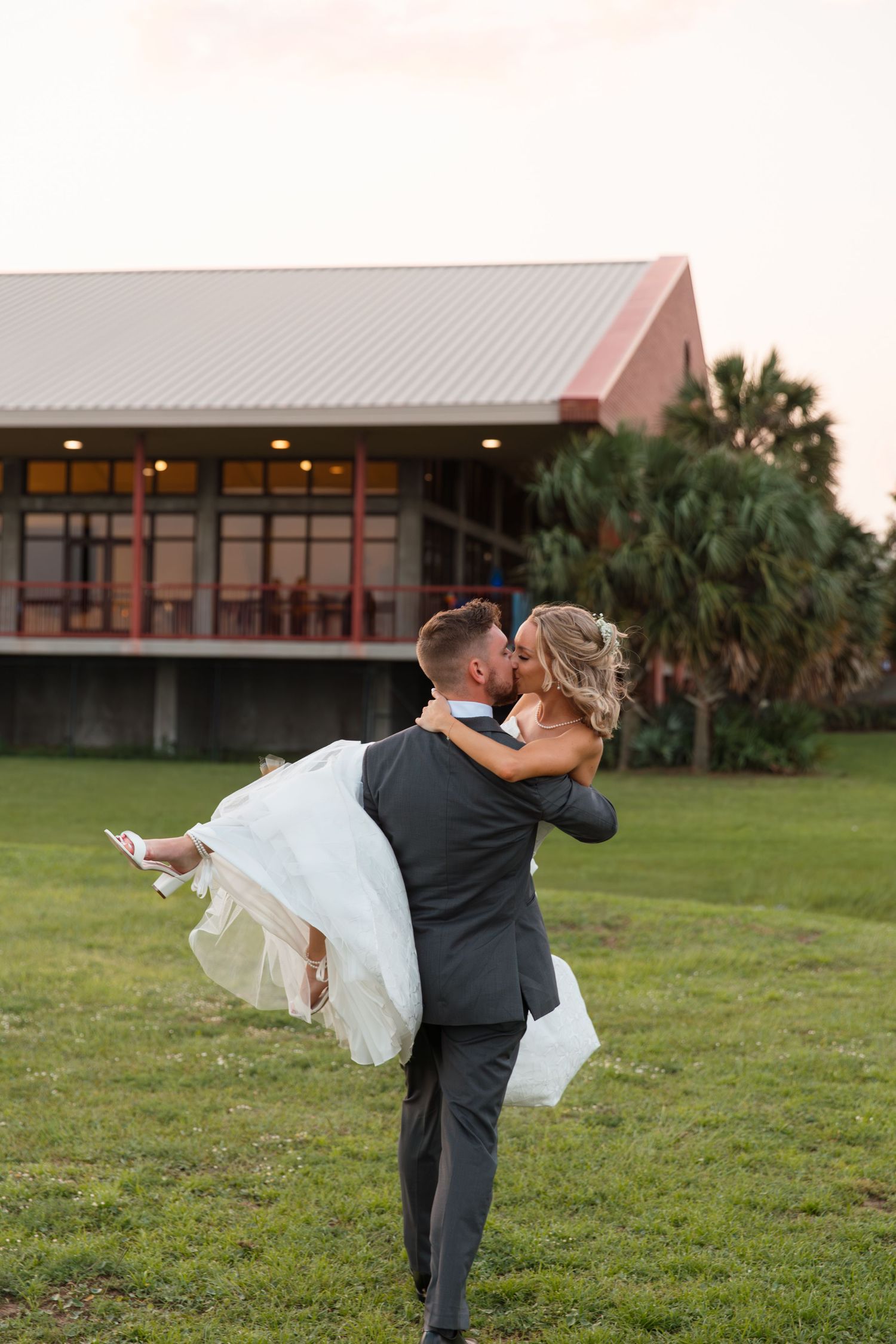 Couple shares romantic moment on grassy lawn with building in background.