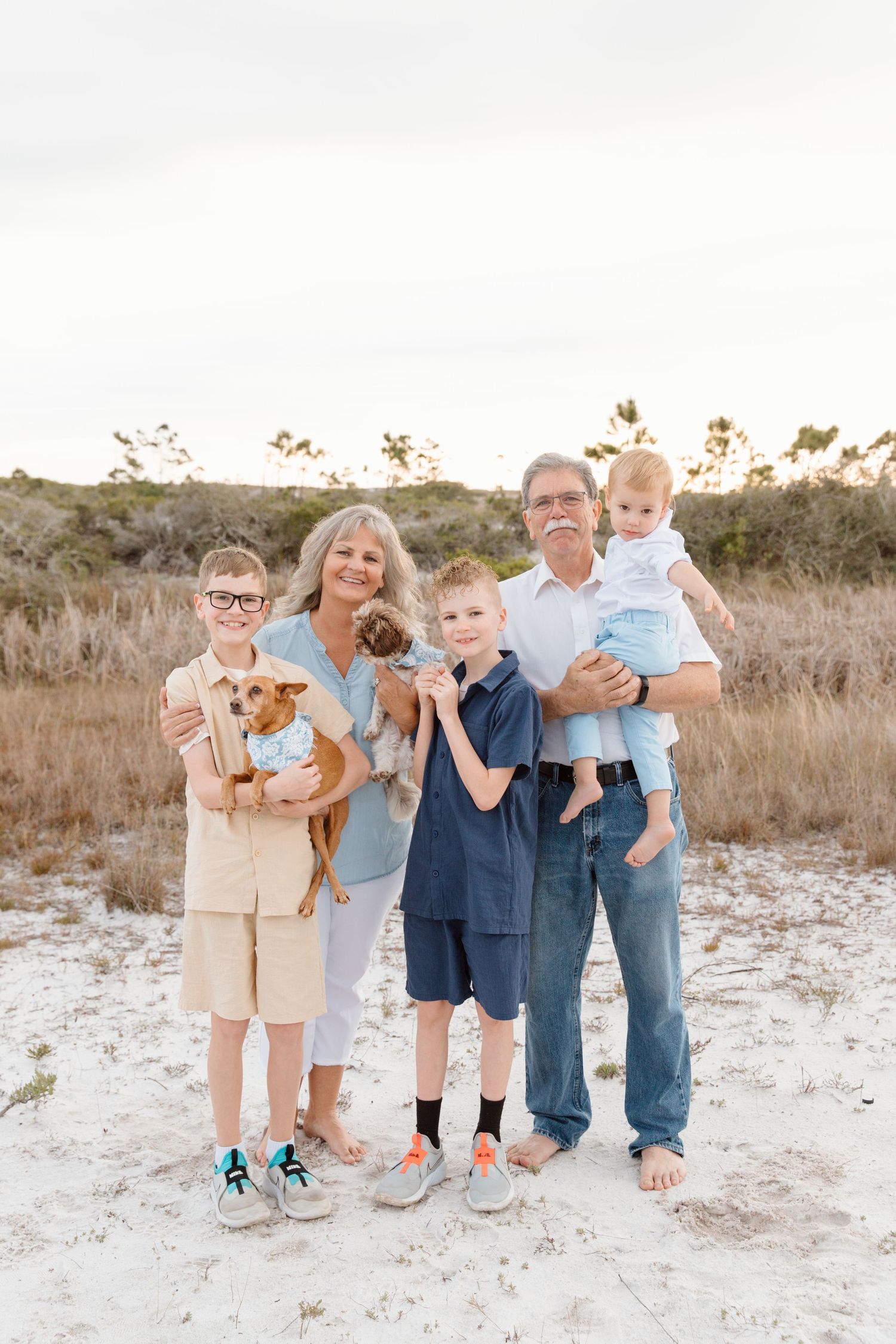 Family poses together on beach with their small dog at sunset.