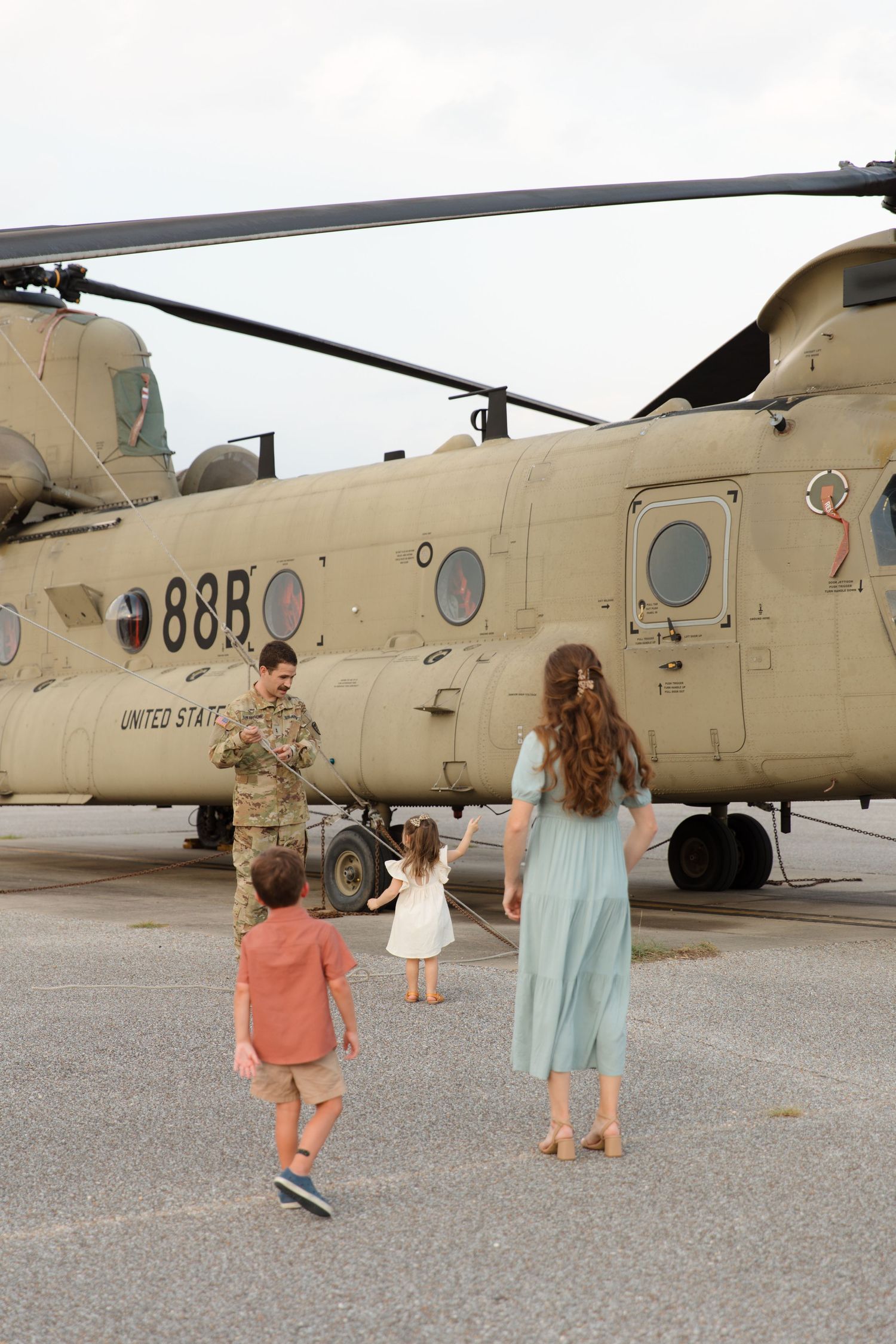 A family walks together near a US Army Chinook helicopter marked '88B' on an airfield.