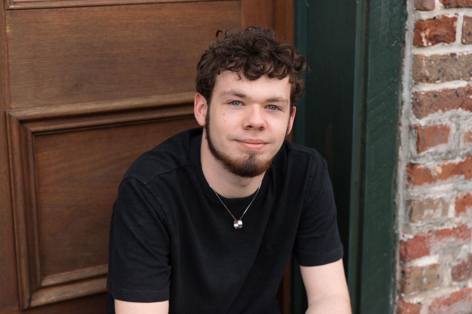 Portrait against wooden door wearing black t-shirt with casual expression.