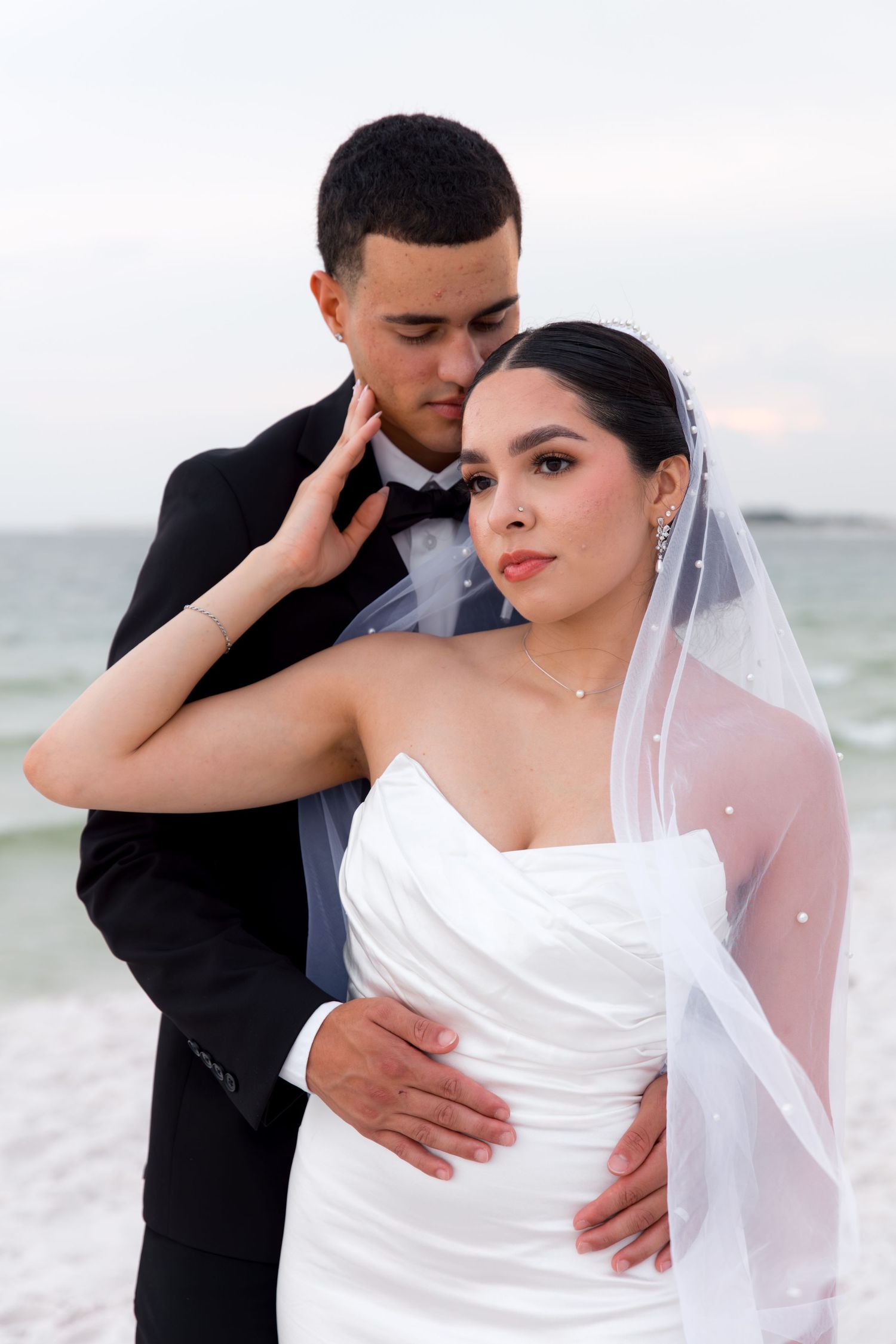 Intimate beach wedding portrait with couple in elegant formal attire.