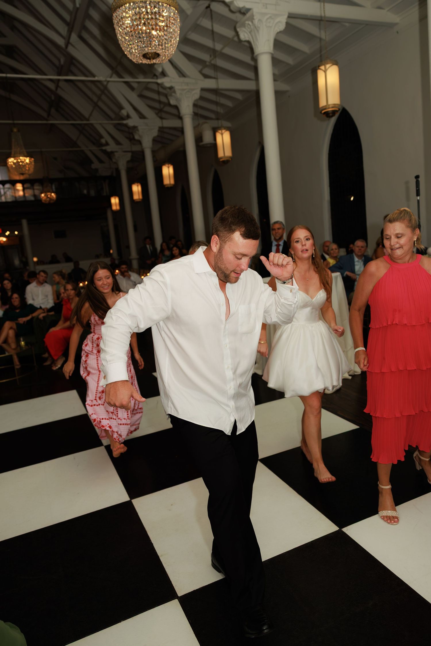 Energetic guest in white shirt dancing on black and white checkered floor at lively wedding reception.
