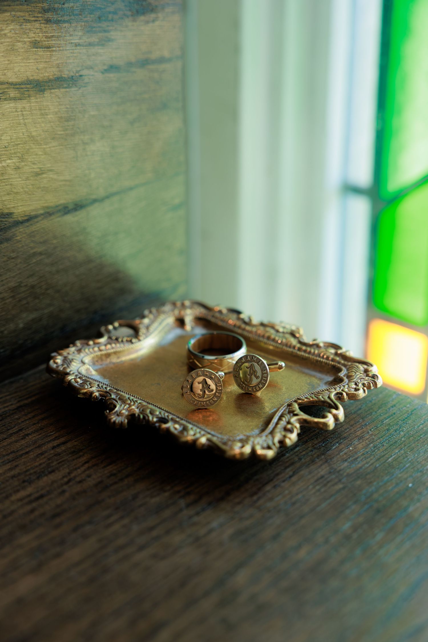 Ornate vintage silver tray holding two antique coin rings near a stained glass window.