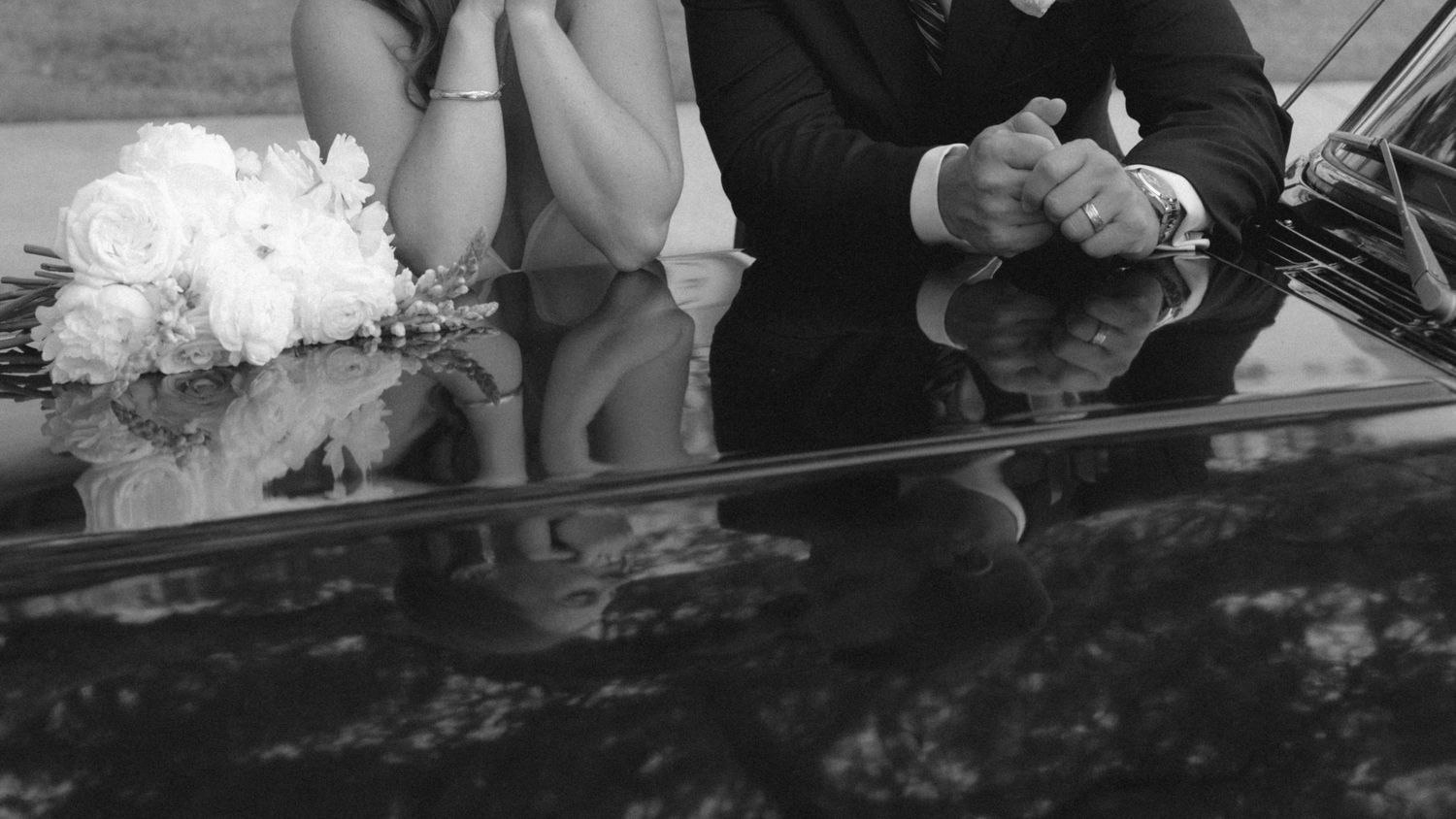 Black and white photo of a bride and groom sitting together, bride holding a white floral bouquet.